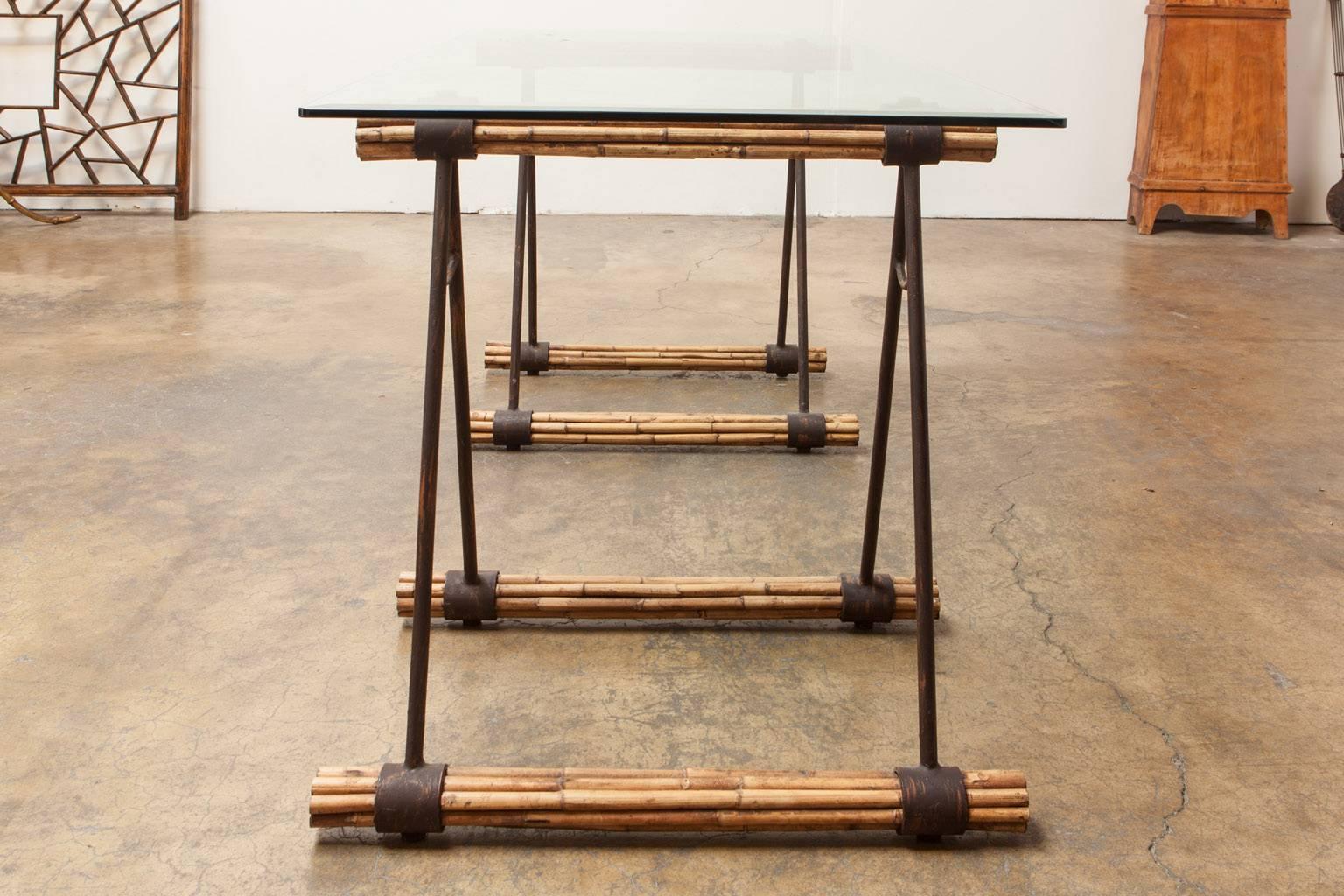 Stylish glass top desk featuring bamboo and iron supports made in the shape of saw horses. The Industrial style is softened with the use of bamboo reeds that also heighten the architectural look of this desk. Topped with a thick pane of beveled