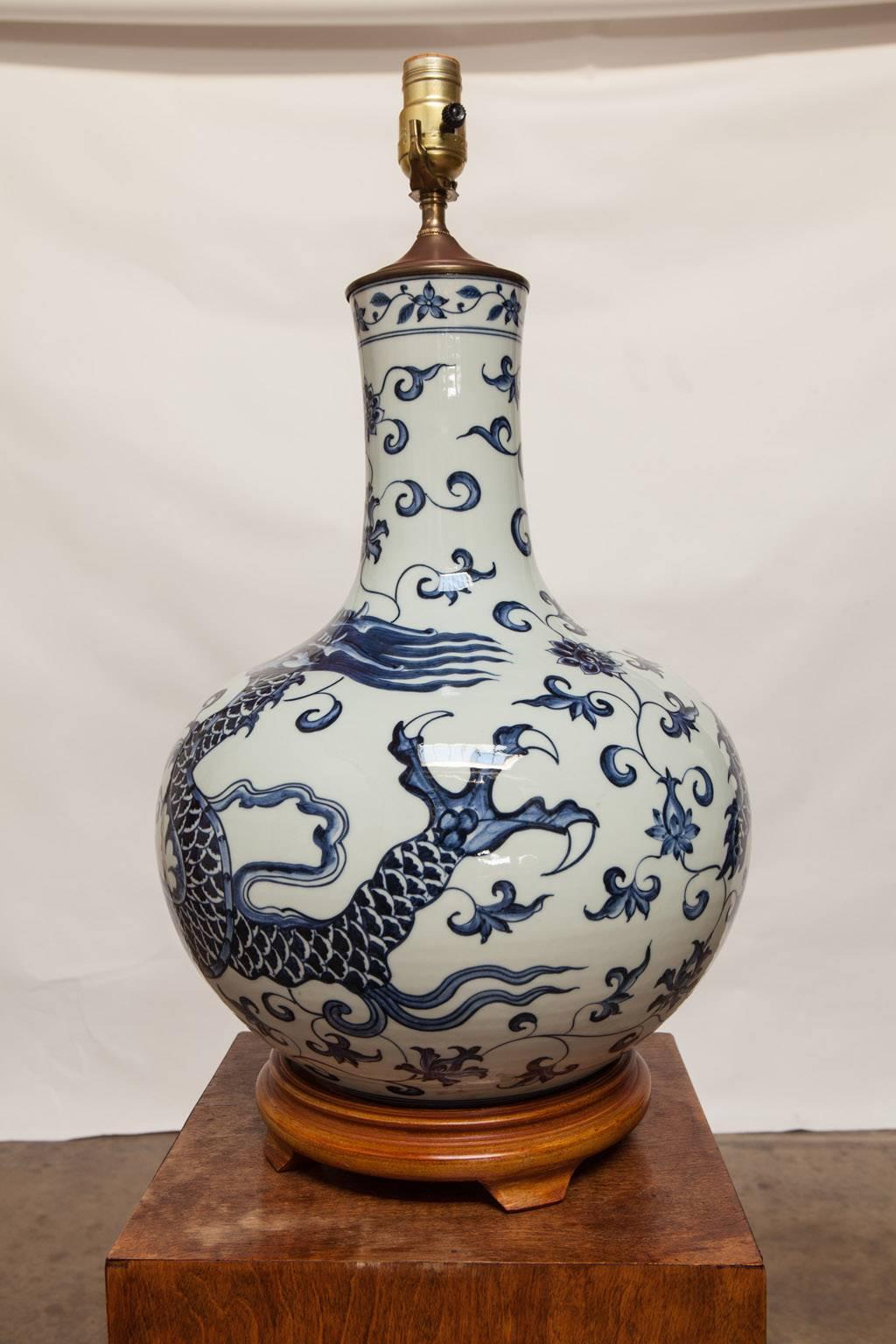 Impressive blue and white Chinese porcelain vase featuring a dragon converted into a table lamp. Supported by a carved wooden base and topped with a brass cap and hardware. Does not include a harp, shade, or finial. Large bulb form body with a