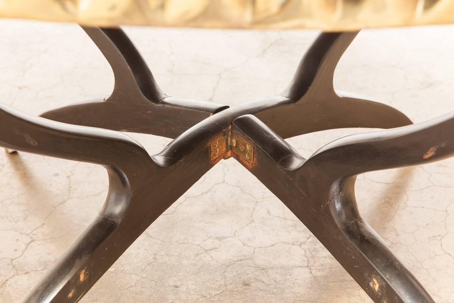 Splendid middle eastern brass tray table supported by a folding spider style base finished in black lacquer with brass feet. Features intricately etched foliate designs on the polished surface and has mounts on the bottom to display on a wall.