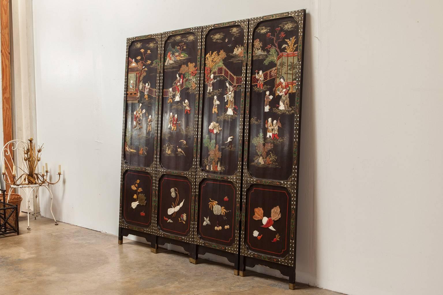 Intricate Chinese four panel Coromandel style screen featuring idyllic scenes made of hand-carved inlay. Decorated with hard stones, coral, jade, bone, and mother-of-pearl on a black lacquer ground with gilt borders and red lacquer highlights. The