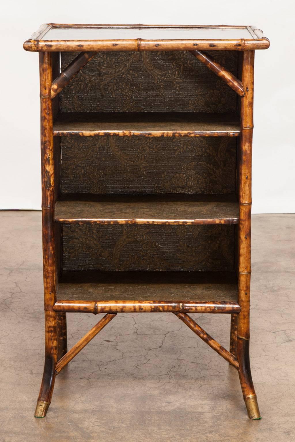 Fabulous pair of English scorched bamboo bookcase cabinets or shelves featuring a lacquered top. Each cabinet has three shelves and appear to have been restored recently to their former glory. The bamboo has a scorched or tortoise shell finish and