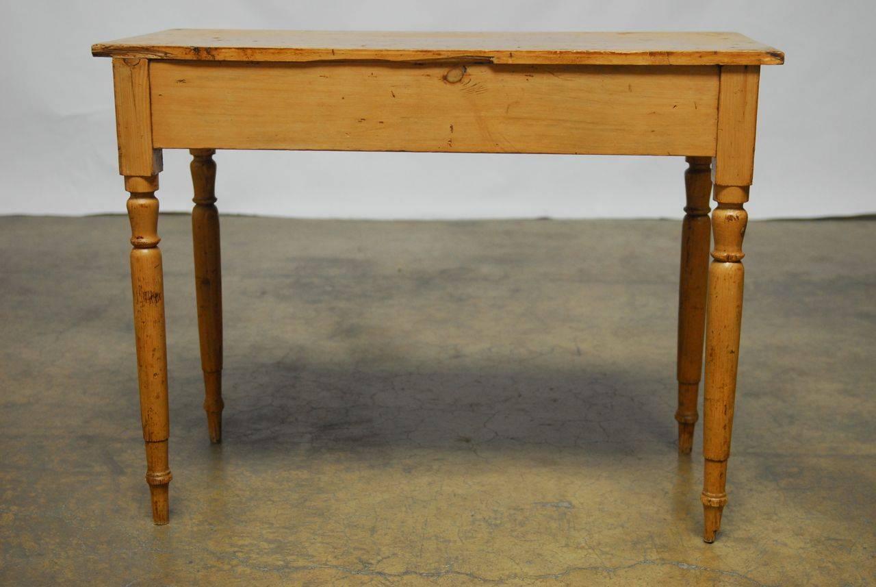 Lovely French country pine console or work table featuring a distressed finish and supported by delicate turned legs. Stabile and solid this diverse table could also be a diminutive desk or writing table. The pine finish not only has the correct