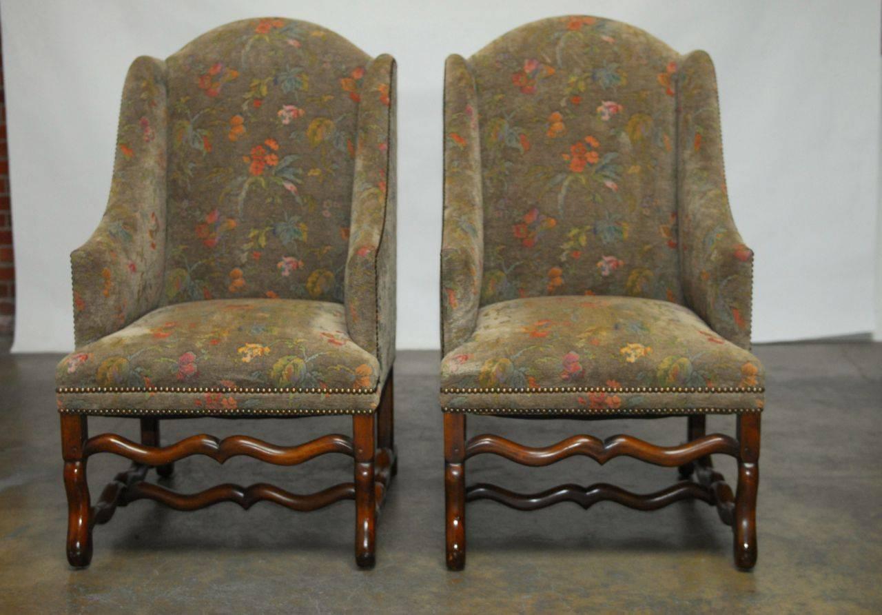Stunning set of carved walnut Os de Mouton style wing chairs upholstered with a Belgium floral tapestry. Features an oversized mutton leg base that give these chairs a whimsical sled look. Custom-made by Formations in Los Angeles, CA. These chairs