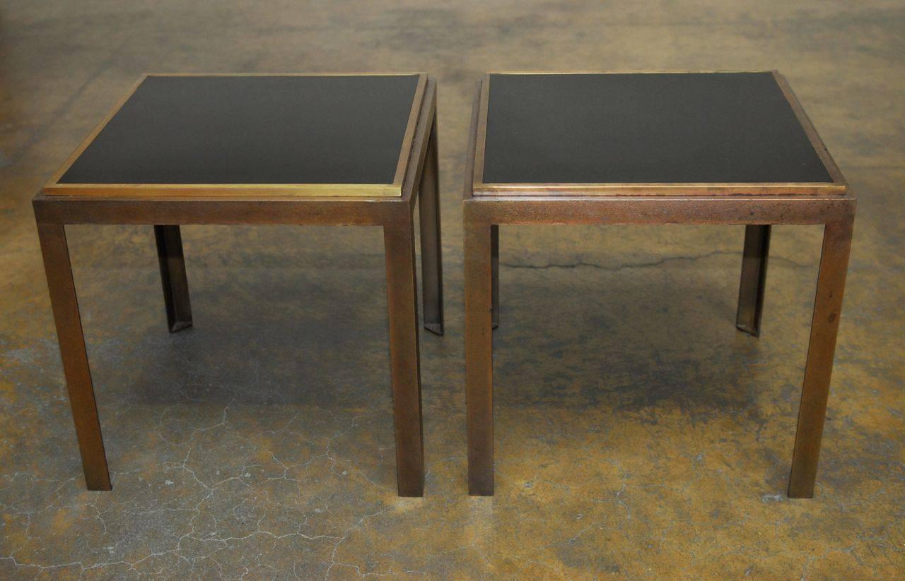 Stylish set of end tables featuring an iron frame finished in bronze with a black Formica laminate top bordered with a brass edge. These tables are cube shaped with quality finishes.