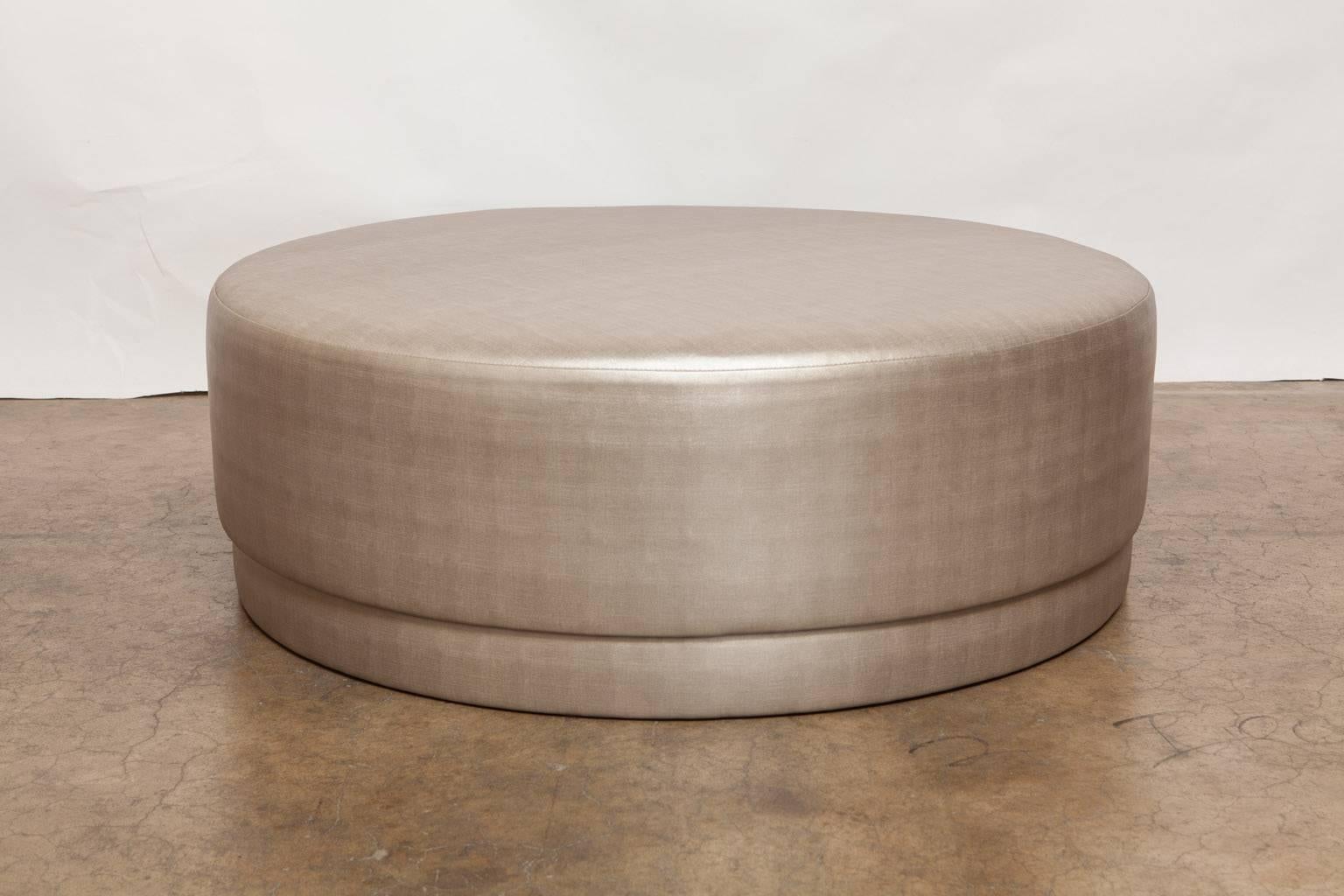 Chic pair of matching round ottomans newly upholstered in a rich textured metallic silver/gold fabric with a gorgeous lustre and feel. Large and generous for casual seating. Pill shaped with padded top and sides.