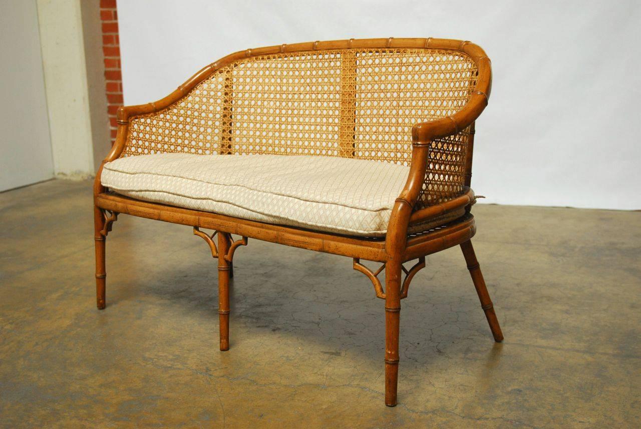 Charming loveseat featuring a carved solid wood faux bamboo frame and cane panels. Made in the Chinese Chippendale taste with five carved legs and decorative spandrels. Removable cushion seat pad features a geometric pattern.