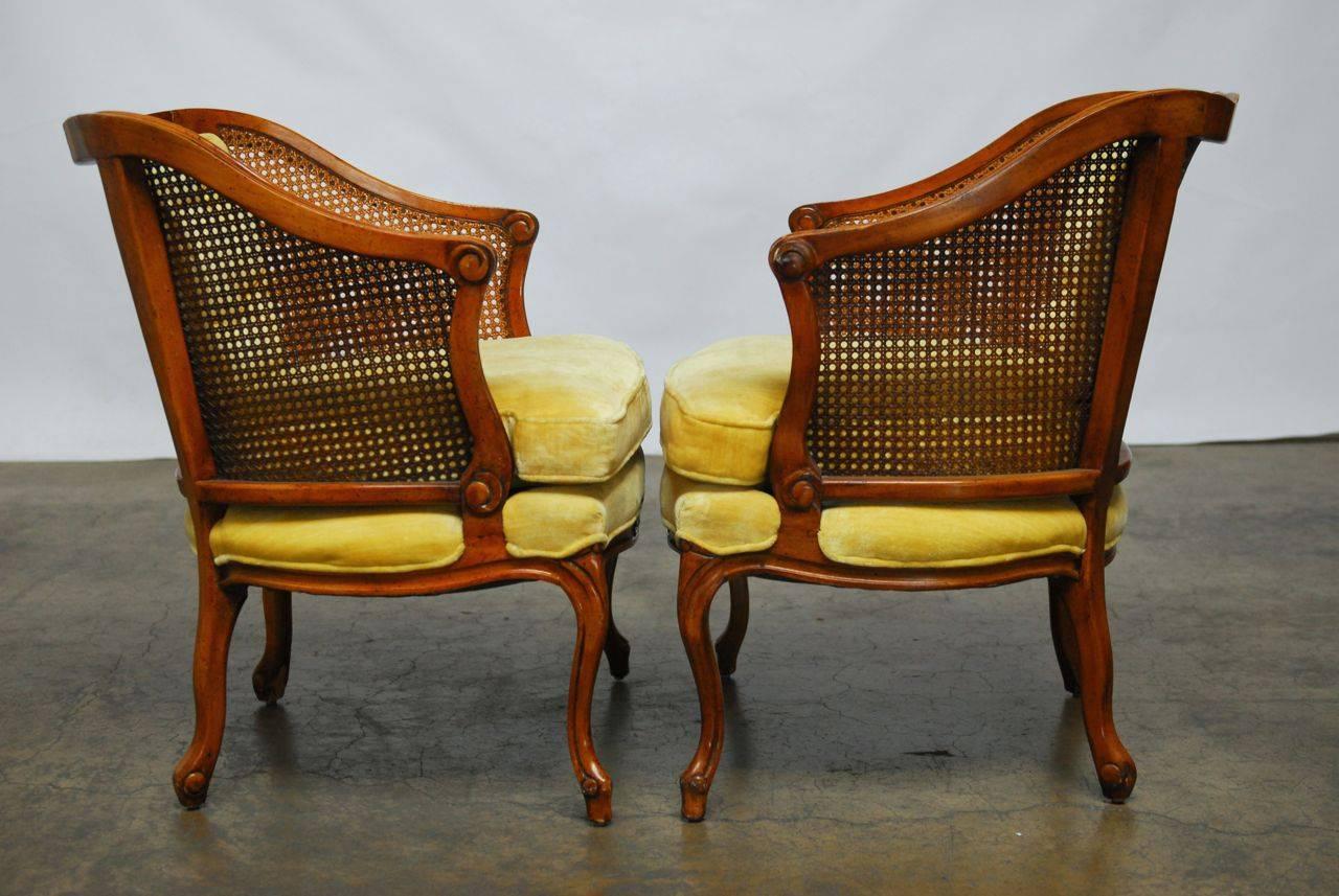 Mid-Century cane barrel armchairs made by Bernhardt featuring a caned back and yellow velvet upholstery. The chairs have a carved crest and molded frames with a loose pillow seat and tufted velvet back. Great candidates for a lacquer update. This