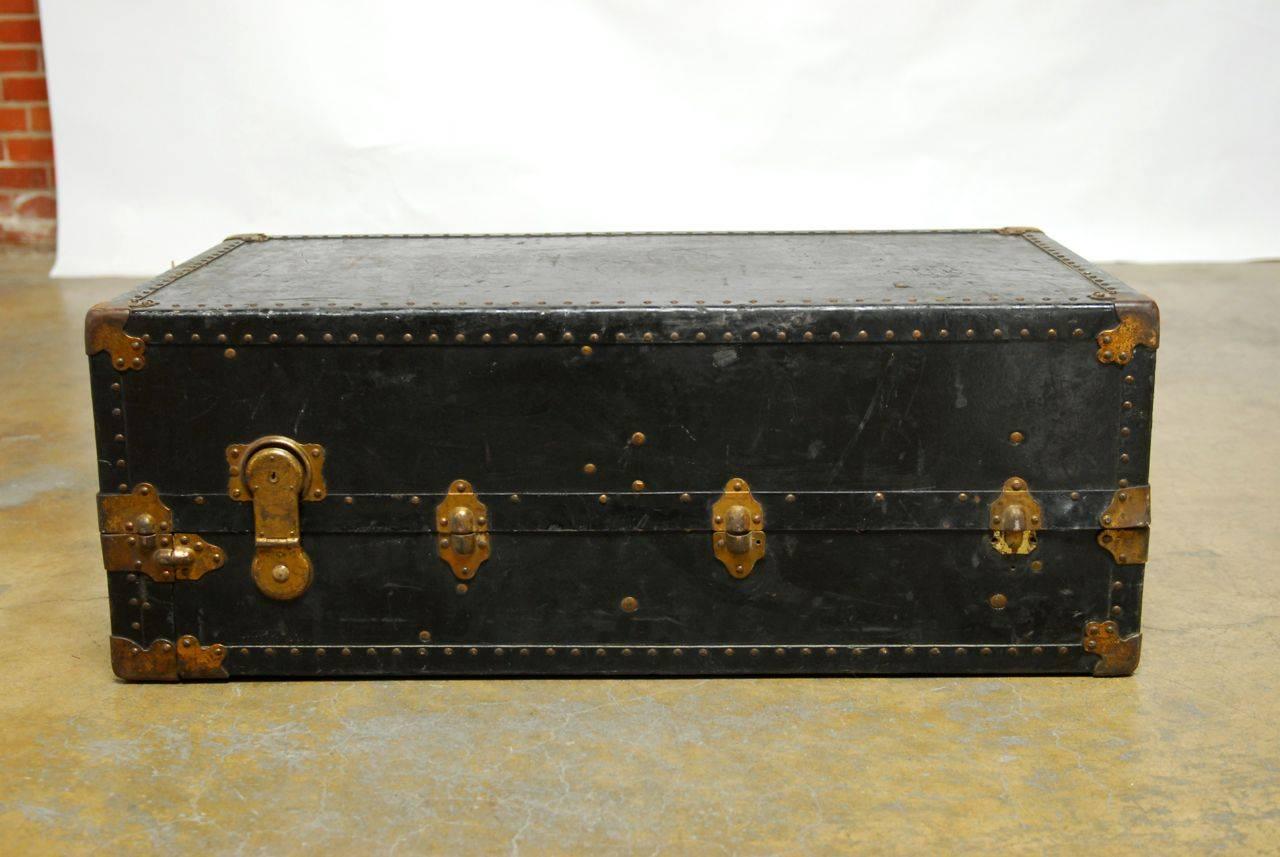 Vintage wardrobe steamer trunk by Oshkosh constructed from their vulcanized fiber with original interior and hangers. Flat top makes an ideal, low-profile coffee table. Still retains its tags and markings from voyages. Well worn and distressed with