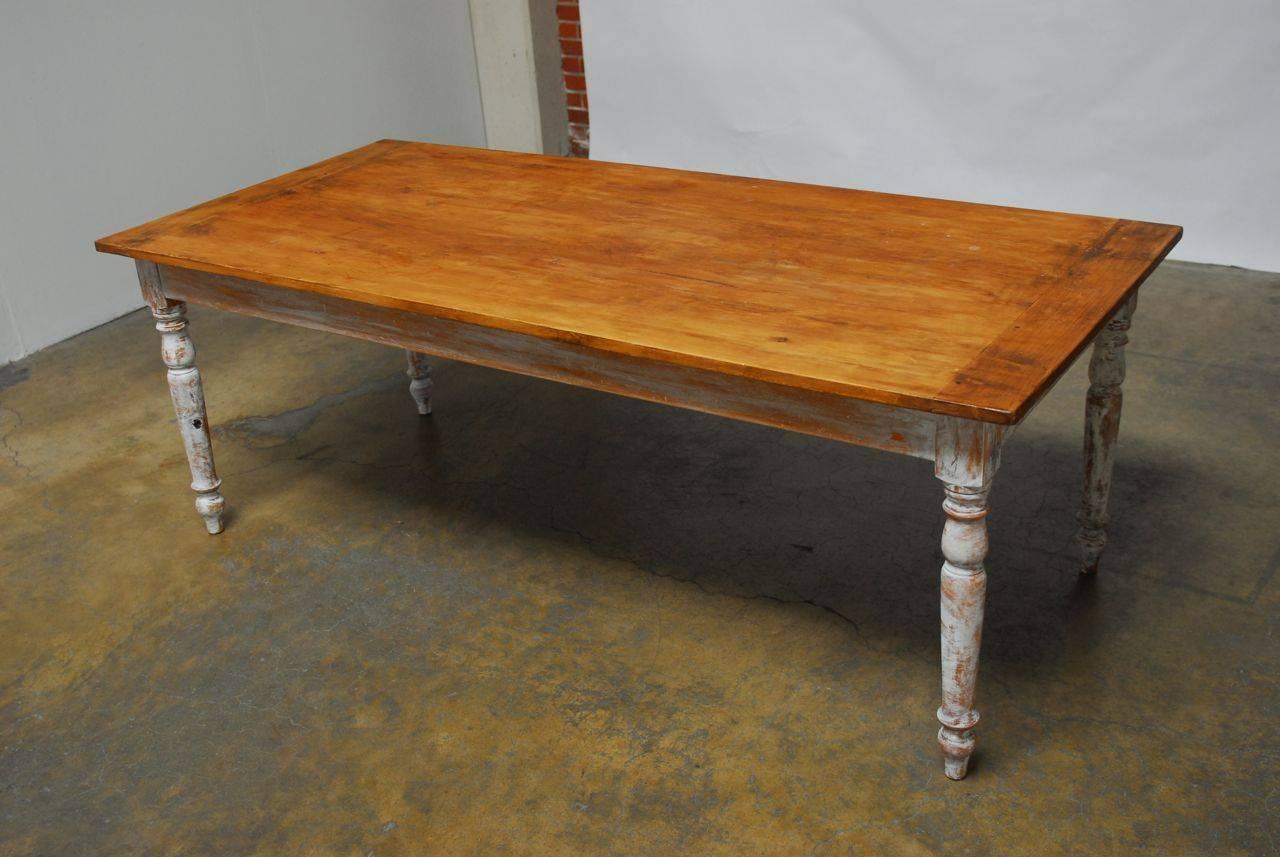 Classic American pine farm dining table featuring a painted base supported by turned legs with toupie feet. Constructed with peg joinery and still retains its original locking drawer with brass hardware. The top has a natural wax finish that