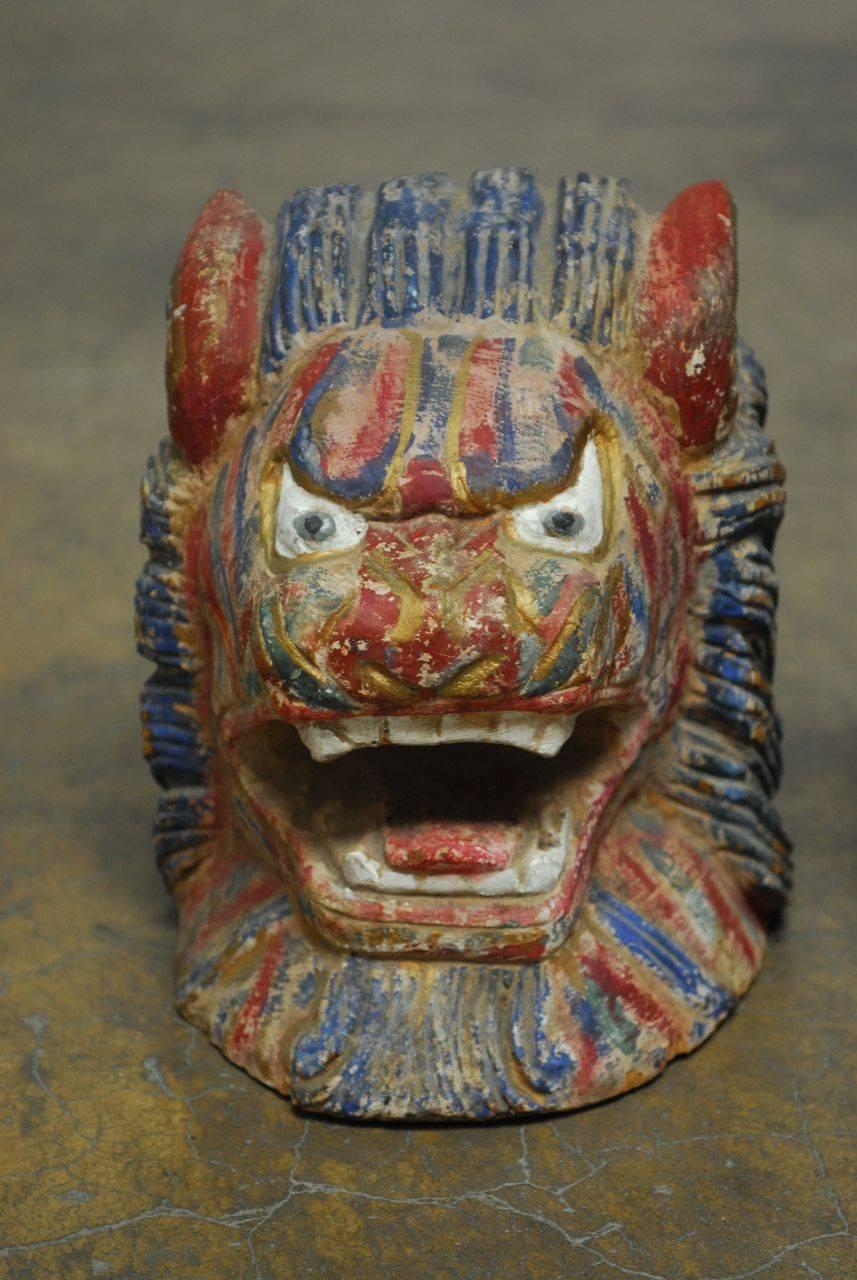Colorful pair of Southeast Asian carved foo dog or foo lion roof ornament heads featuring a polychrome multi-color finish. Fierce expression and flowing hair, each is carved from one heavy piece of heart wood. Originally displayed on an asian