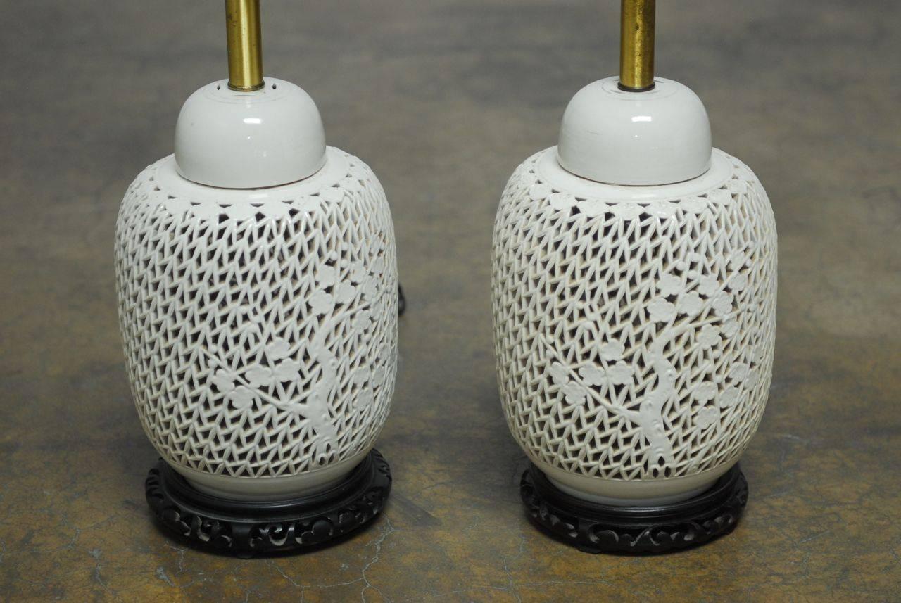Pair of ginger jar form Blanc de Chine table lamps featuring a pierced body with foliate motif and matching lids. These vases are mounted on a carved wooden base and have original brass hardware. No shades included.
