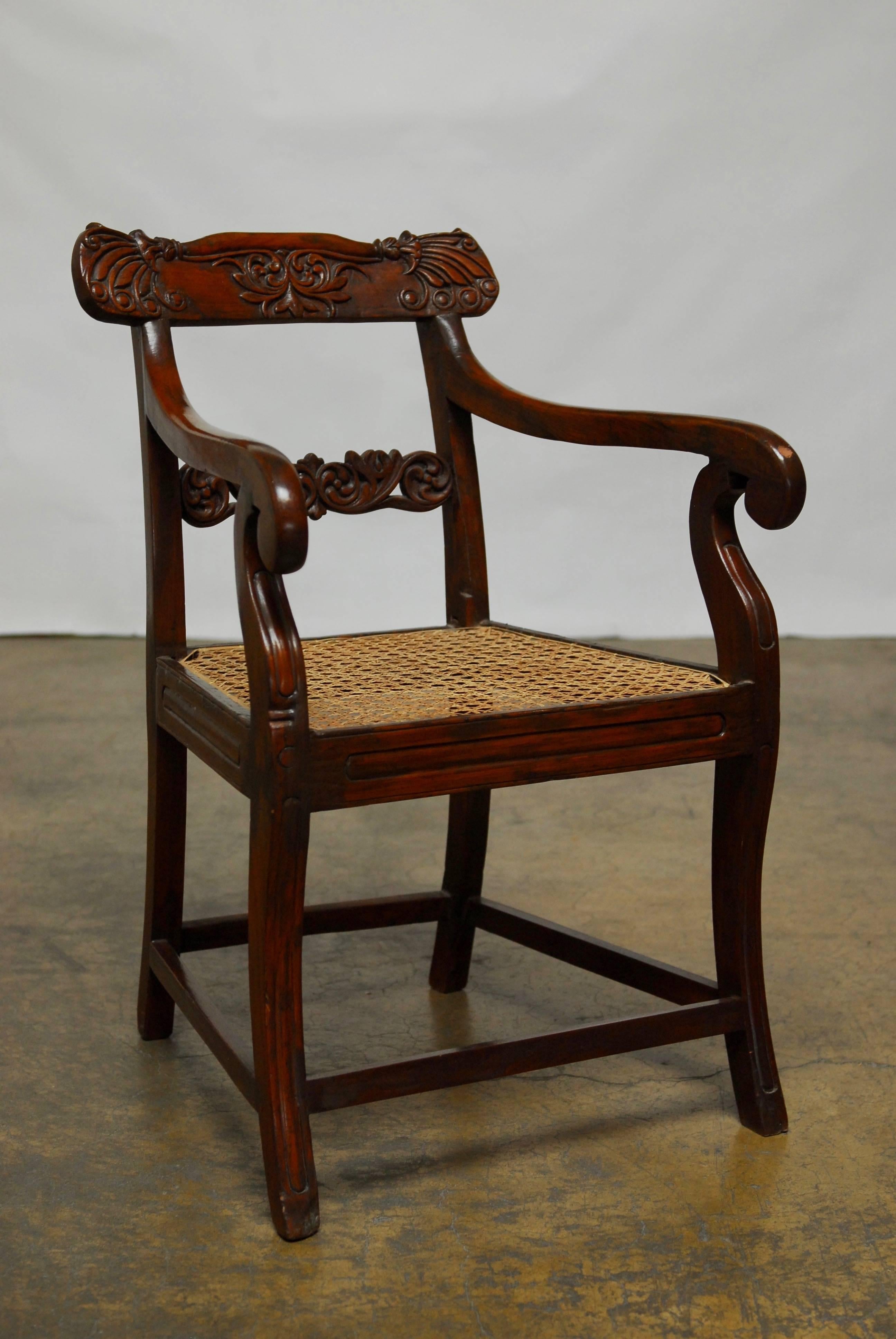 Unique carved rosewood armchair made in the Anglo-Indian or British Colonial taste. Featuring long scrolled arms and a cane seat. Carved back splat and crest supported by square legs and box stretcher. Chair is in very good condition with tight