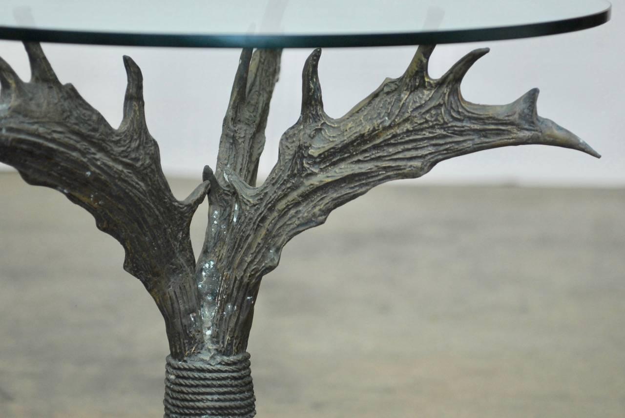 Fantastic faux antler table made of bronze featuring three large stag antlers conjoined with bronze rope and topped with a round glass top. Each crescent shape horn ends with a point and has a patinated bronze finish.