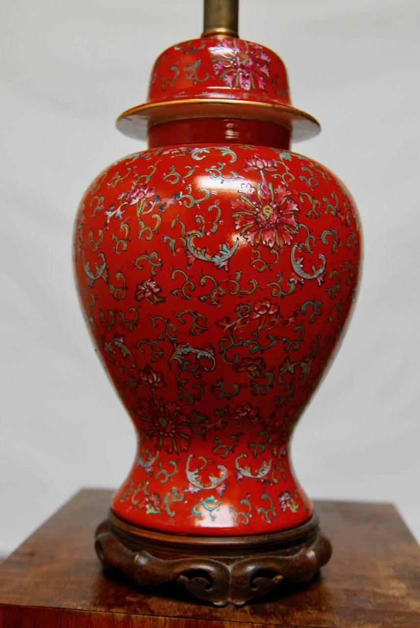 Colorful Chinese red ginger jar converted to a table lamp. Featuring a floral and foliate decorated body and lid. Supported by a carved base with intricate detail. Original brass hardware with harp and finial but no shade. The vase alone measures