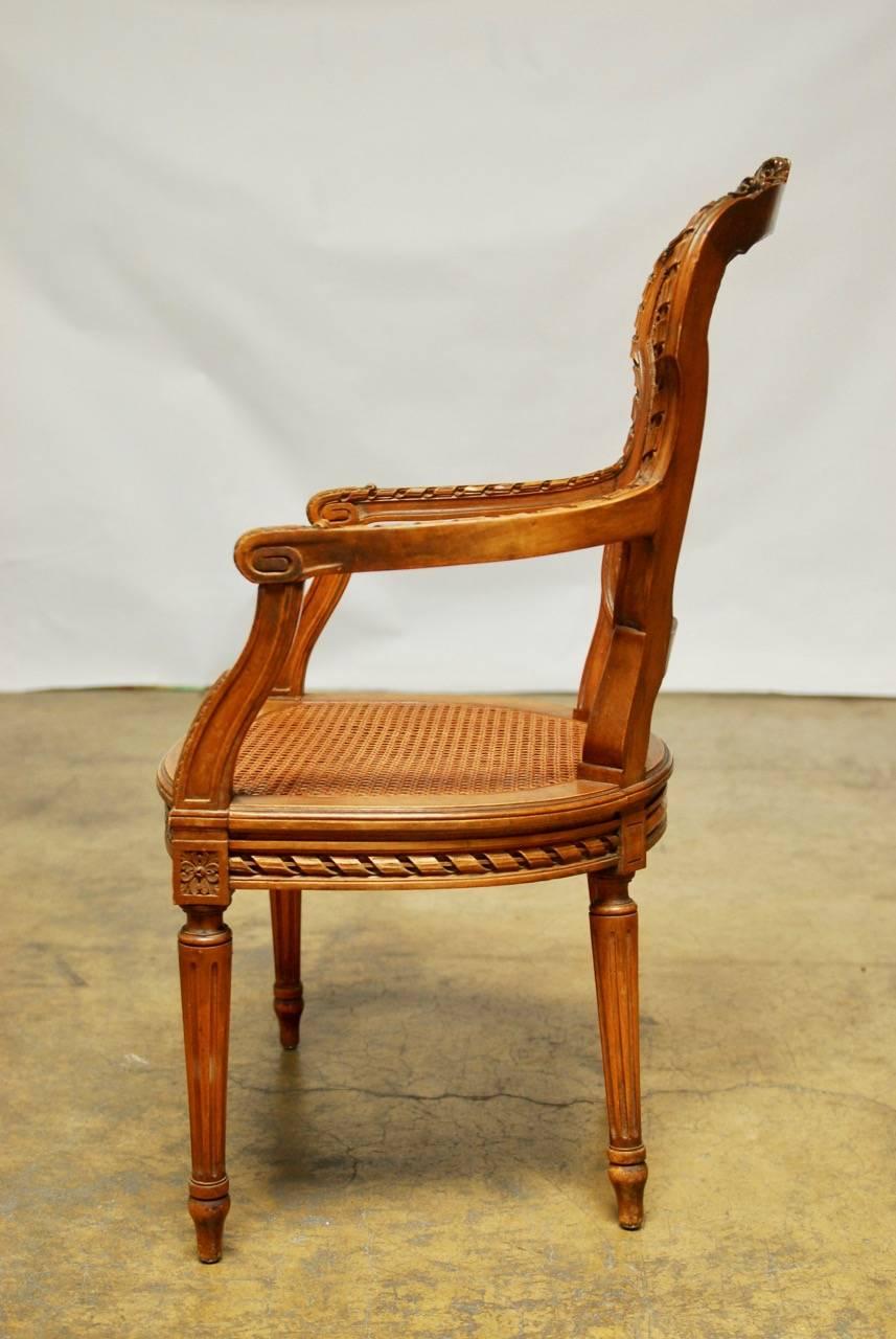 Distinctive French Louis XVI style fauteuil armchair carved in the neoclassical taste featuring a shield backrest. Highly carved and molded frame with a ribbon accent and floral crest. Caned back and seat with carved rosettes. Supported by fluted