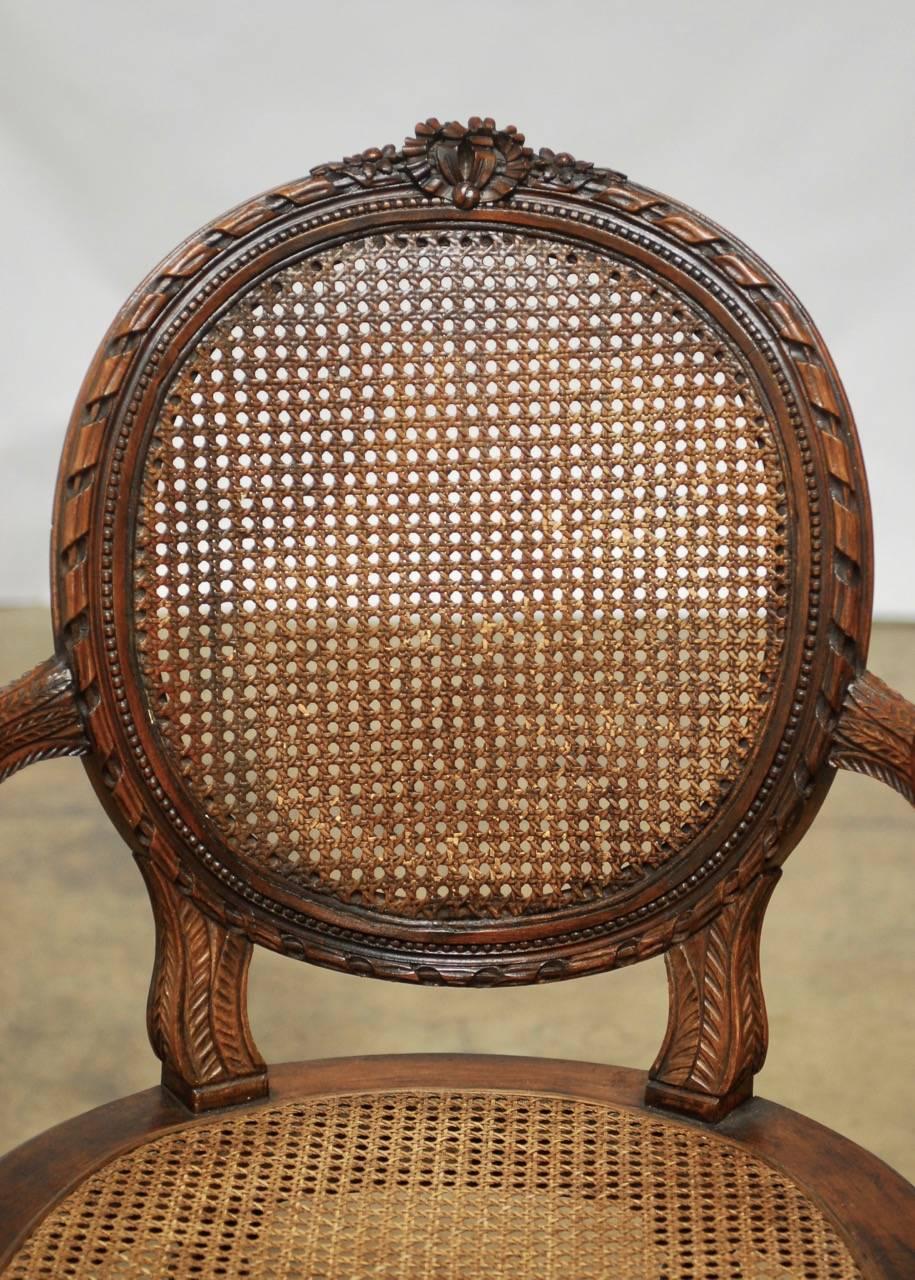Grand neoclassical French, Louis XVI style carved fauteuil armchair featuring a caned round back and seat. Beautifully molded frame with a delicate carved ribbon accent and ribbon wreath on the crest flanked by flowers. The apron has rosettes and is