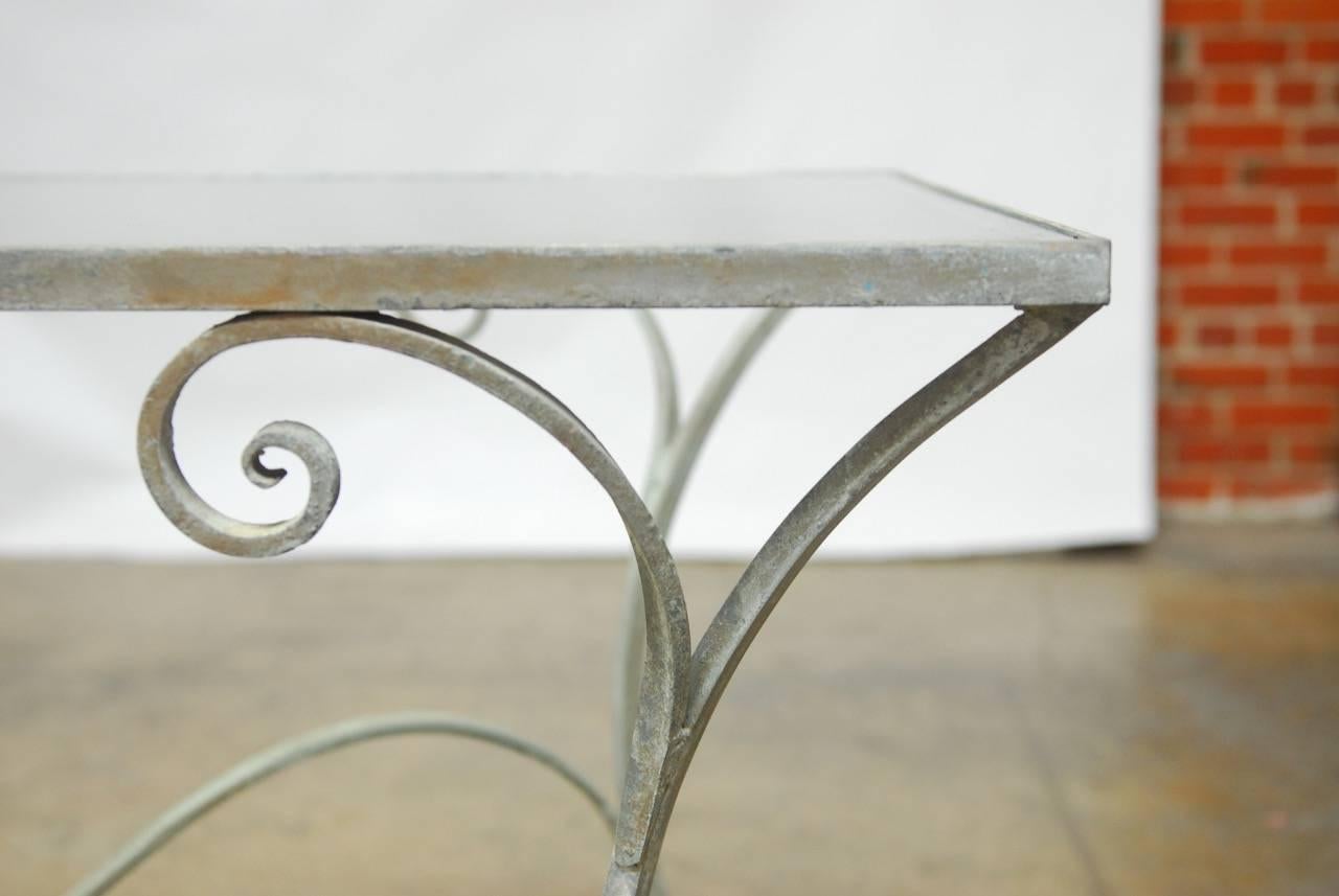 Charming French garden or patio dining table featuring a scrolled wrought iron frame topped by a pane of glass. Beautifully hand-formed stretchers and graceful legs that end with flat feet. The metal has great patination with some paint remnants.
