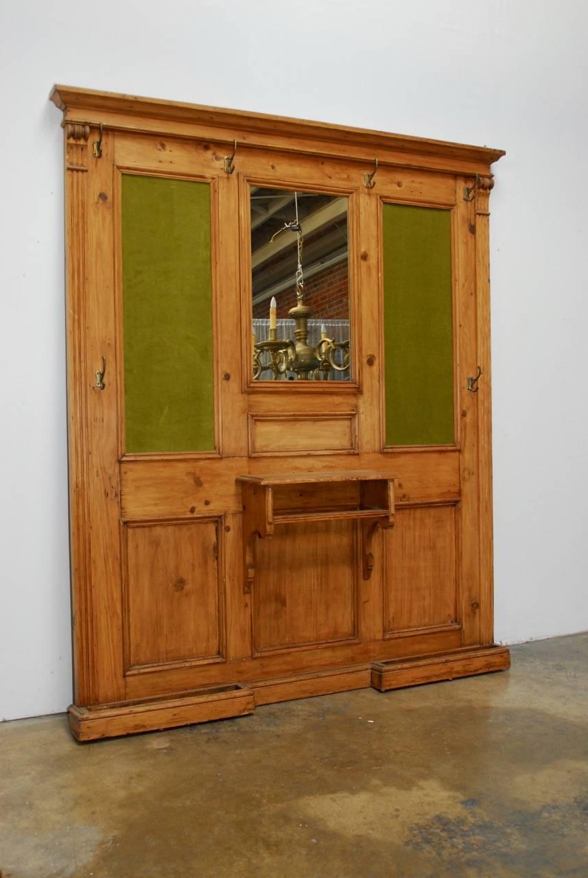 Impressive 19th century French pine entry hall tree or coat rack with mirror. Features a natural finished pine wainscoting and period framed felt panels surmounted by a cornice top. Fronted by a small shelf with a rack and two umbrella drip trays