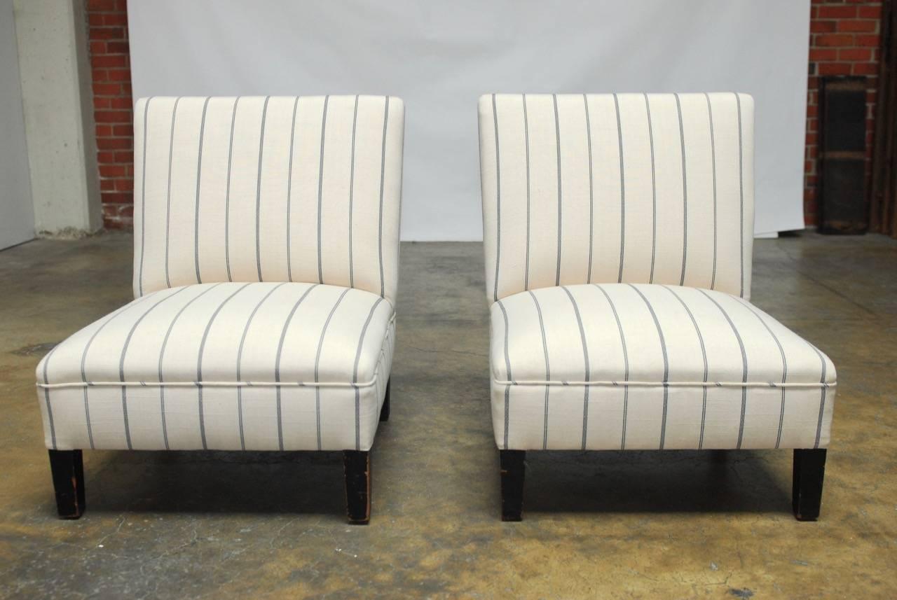 Stylish pair of slipper chairs featuring newly upholstered frames in French linen with a blue stripe. Professionally refurbished with new padding and bordered with an angled welt. Supported by square legs with a distressed ebonized finish.