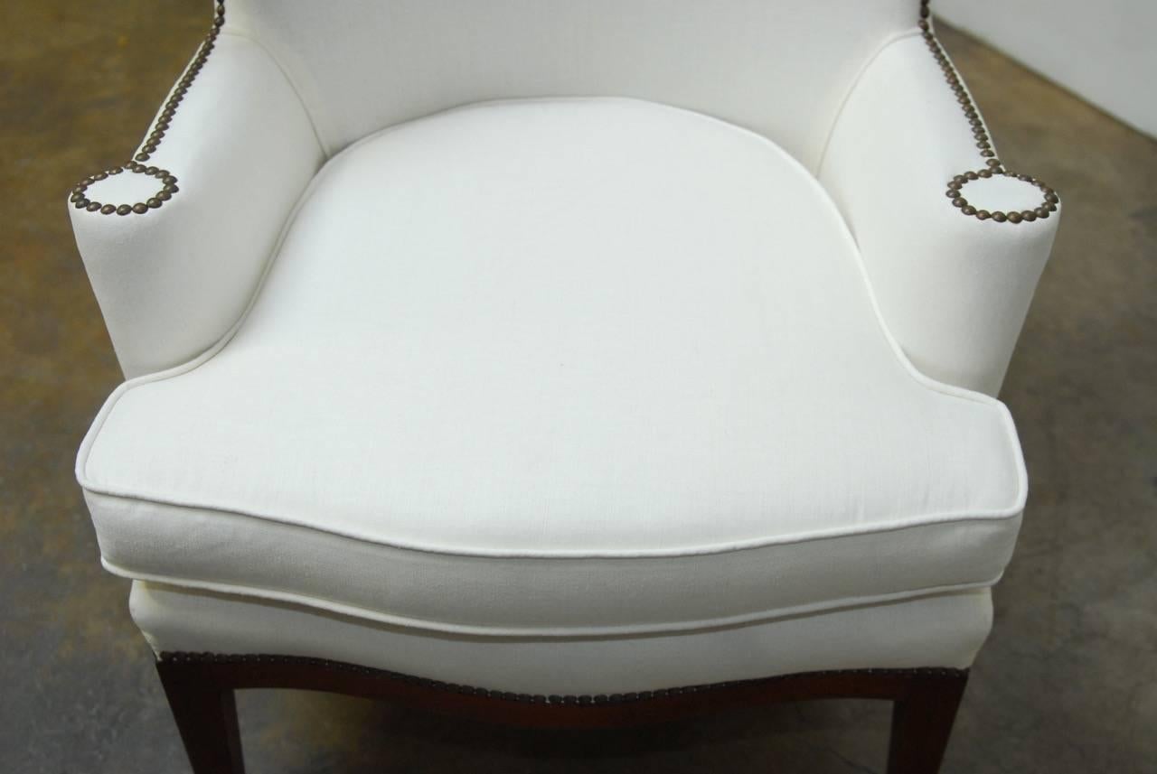 Iconic early wingback armchair designed by Edward Wormley for Dunbar. Featuring a newly upholstered frame finished in an organic white Irish linen. Accented with brass nailhead trim and supported by a mahogany base with tapered legs. Professionally