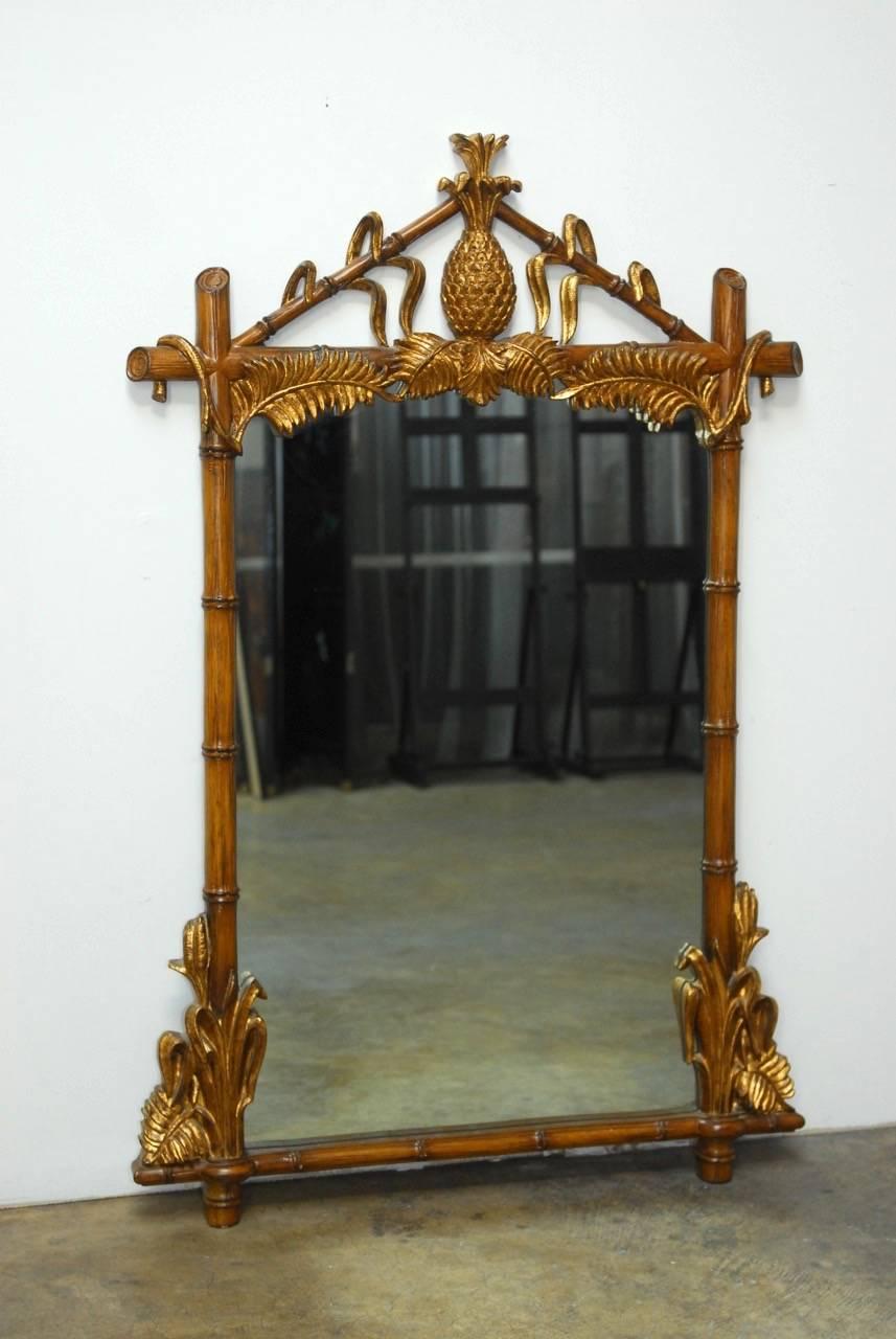 Fabulous faux bamboo wall mirror made in the Hollywood Regency style decorated with palm fronds and surmounted by a gilt pineapple.