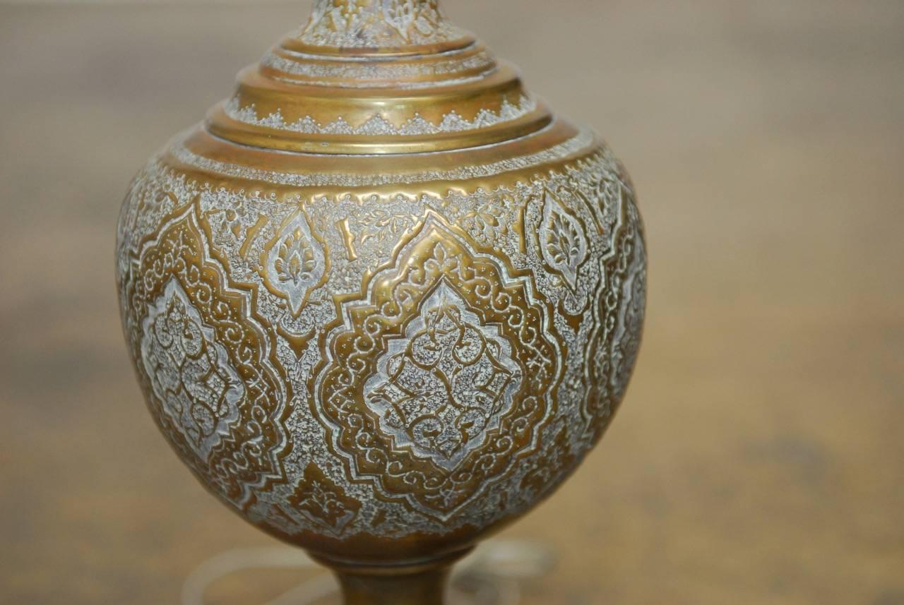 Elegant Mid-Century Persian hand-etched brass lidded urn mounted as a table lamp. Intricate Indo-Persian decoration on the tall urn with a trumpet style neck mounted on an ebonized and pierced wood base from China. The brass harp has an adjustable