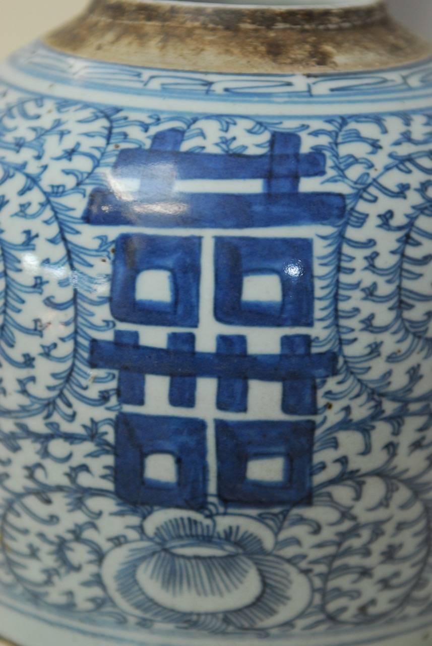 Chinese blue and white jar featuring a Shuangxi emblem amid a field of floral sprigs and flowers. Intricately hand-painted with a short rounded neck and no lid. Beautifully faded with an aged patina.