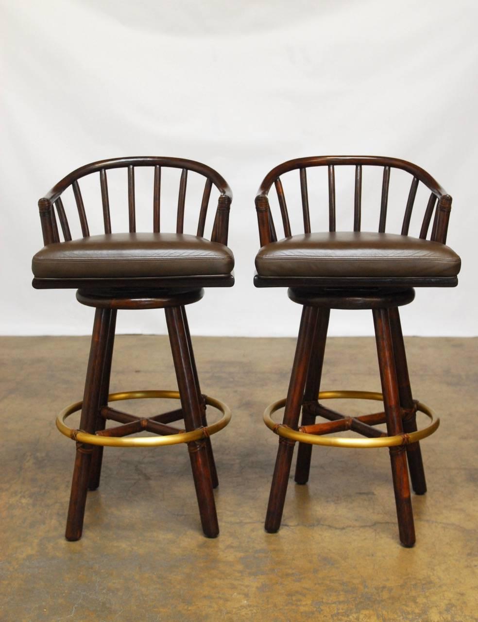 Handsome pair of bamboo and rattan barstools by McGuire featuring swivel leather covered seats. These barstools are made with the famous McGuire rawhide strapping and Classic brass foot rail. Finished in a rich chestnut color with matching leather