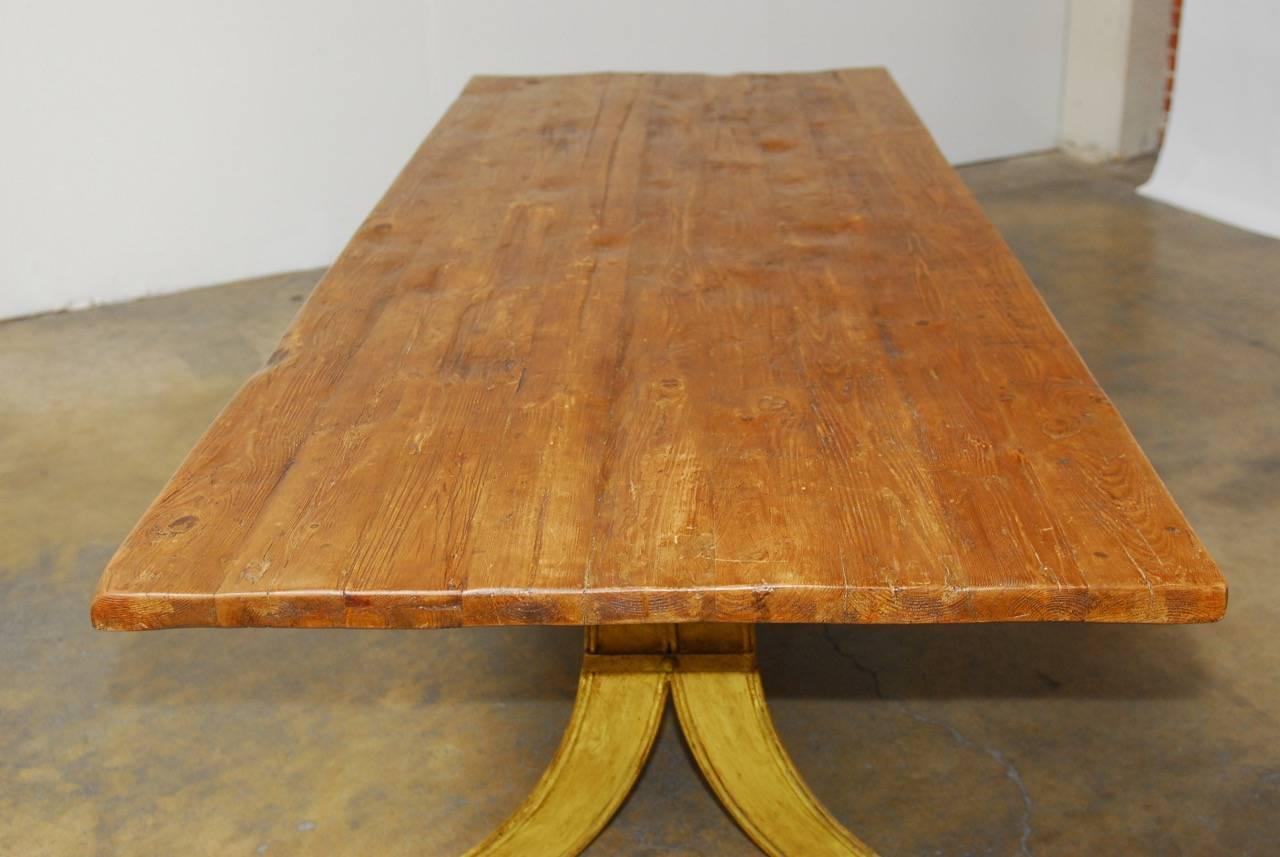 Impressive French dining table featuring an Industrial iron base with splayed legs. The base has been painted and has a distressed yellow finish. The top is constructed from hand-hewn planks made in a farm table style. The table is very heavy and