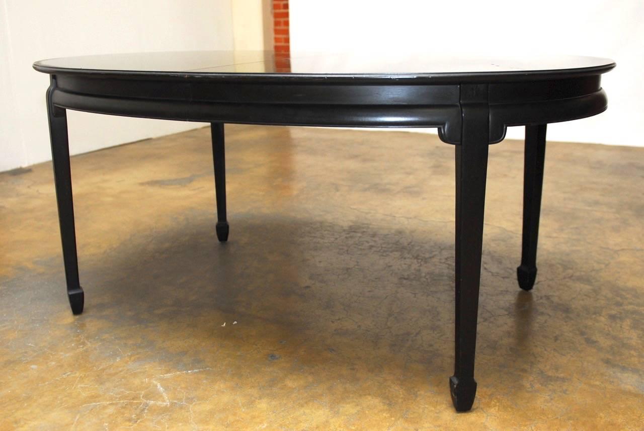 Black lacquered oval dining table made in the Asian taste attributed to Baker's Far East collection of furniture. Mid-Century style featuring a floating top and supported by tapered legs with chow feet, or spade feet. Original 