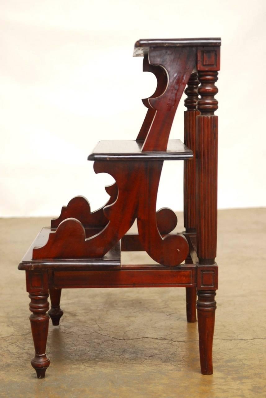 Handsome solid mahogany library steps made in the Regency style with three steps supported by tapered legs and a reeded column back. Beautifully carved with decorative accents and a rich finish.