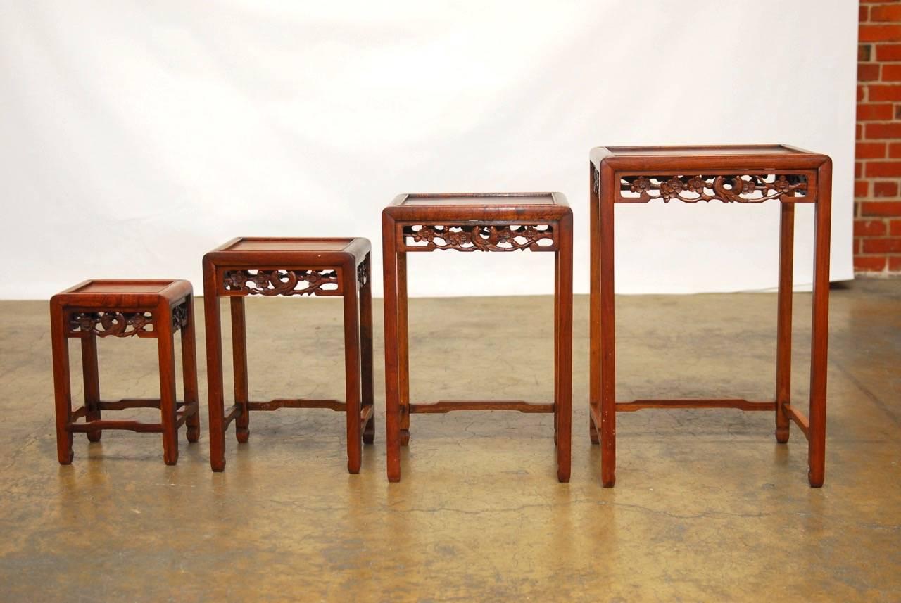 Set of four Chinese rosewood nesting tables each featuring hand-carved decoration of birds and flowers on all four sides. Conjoined on three sides with humpback stretchers and showcasing the rich finish with interesting grain patterns.