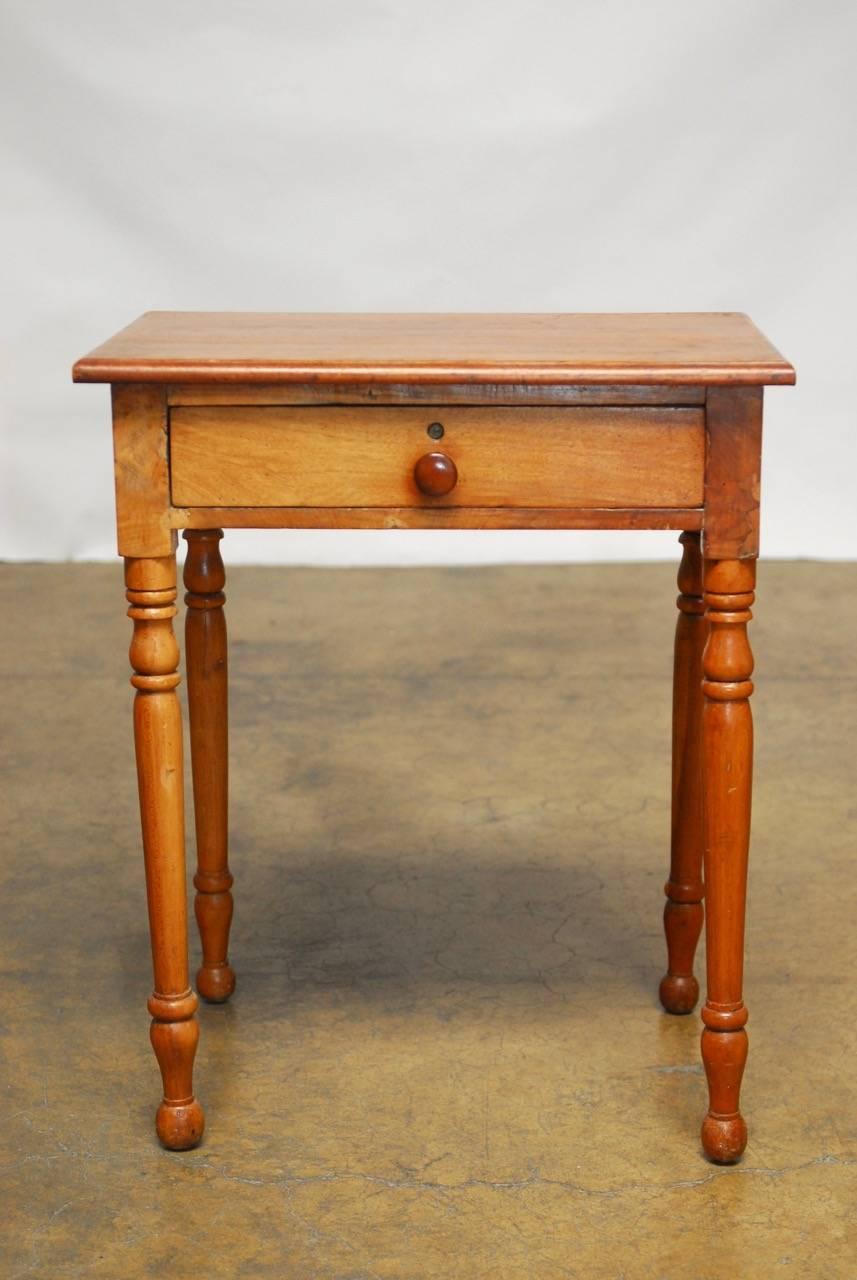 Diminutive farm table or desk made in the Federal style constructed from mahogany with a single drawer front. Features long turned legs with a lovely rustic patina on the vintage wood. Dove tail drawer with locking hardware and no key. Small enough