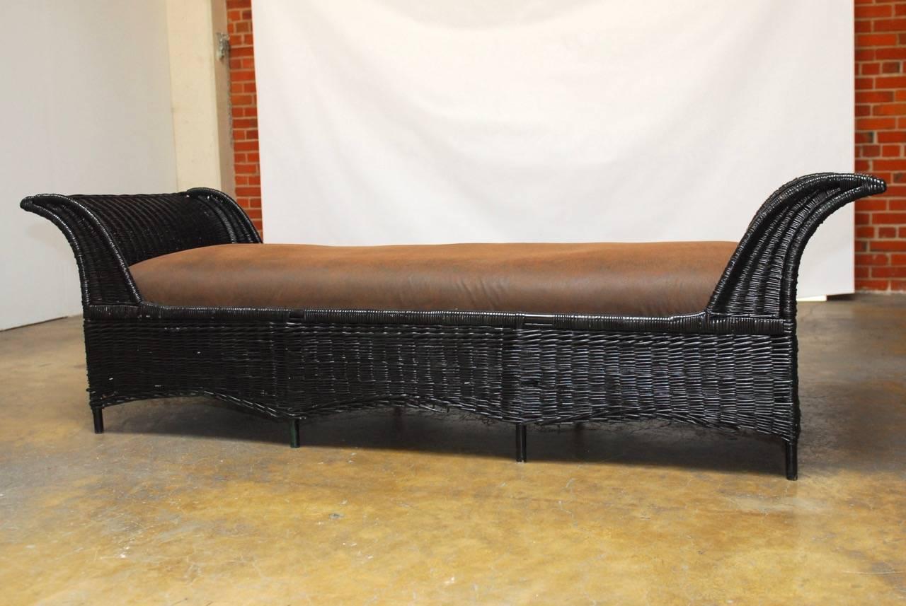 Stylish black lacquer wicker daybed featuring graceful curved ends and upholstered with a faux leather fabric. The frame is covered in wicker with a scalloped apron and is supported by eight legs. Originally green the entire frame has been updated