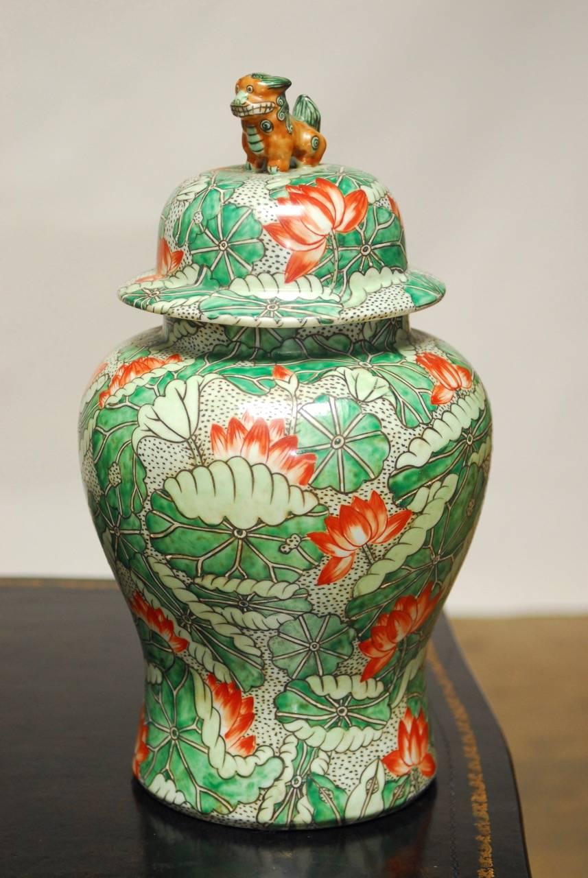 Stunning pair of temple ginger jars featuring fern green and red lotus blossom decoration. Both lidded urns have foo dog or foo lion finials with expressive faces. Each having a 