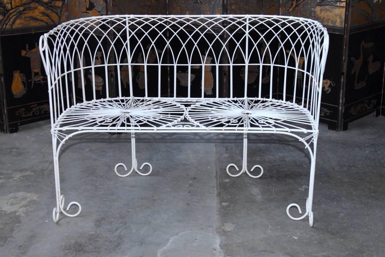 Fantastic set of French wrought iron and wire garden patio set consisting of two round back armchairs and one settee. These pieces feature wrought iron frames with extensive wire work designs of scrolls and sunbursts. Supported by fancy curled feet