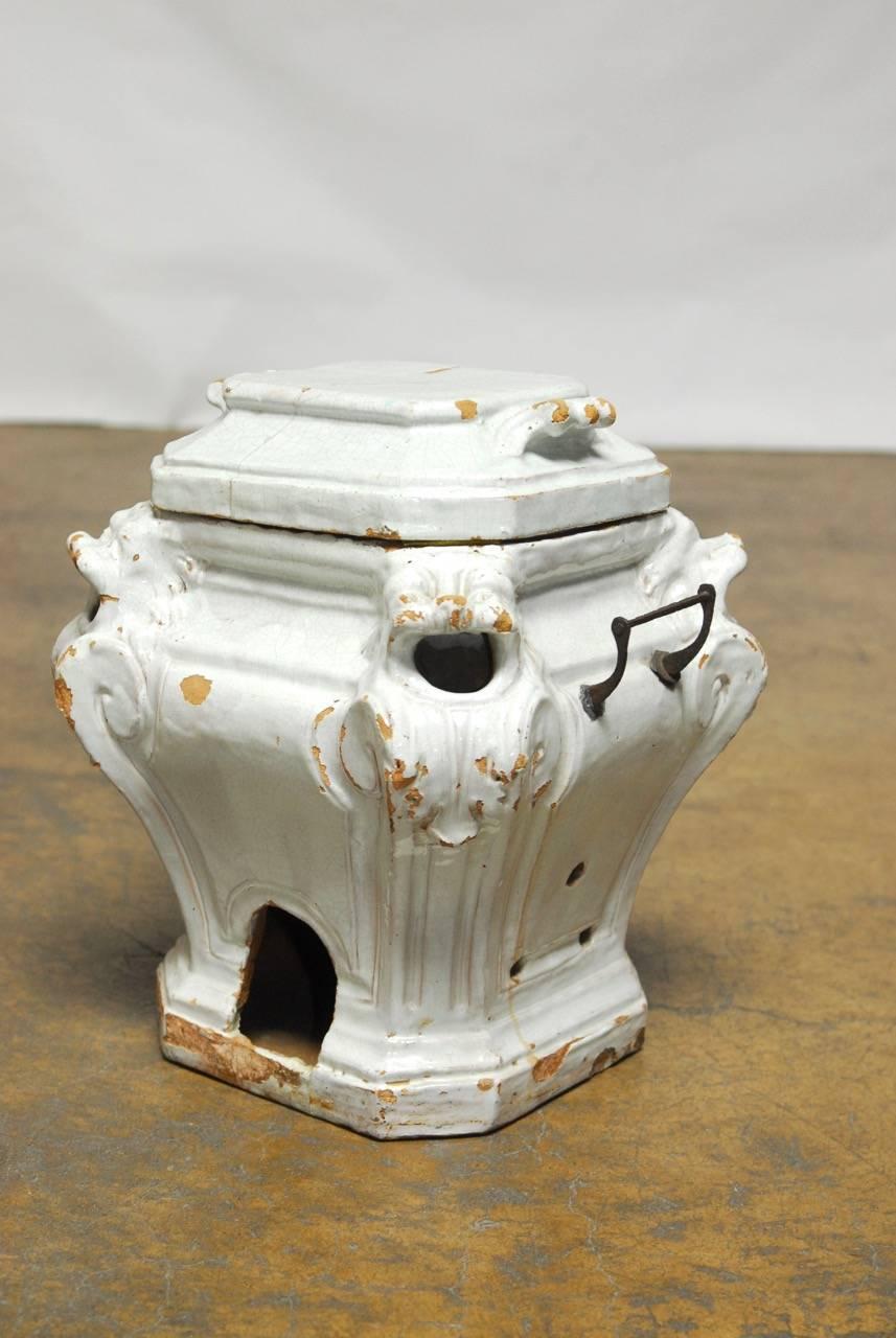 Featuring a large lidded body decorated with lion heads on each corner depicted with open mouths where heat escapes. This thick glazed ceramic urns has openings on each side large enough for hands and holes to ventilate air in the sides. Several