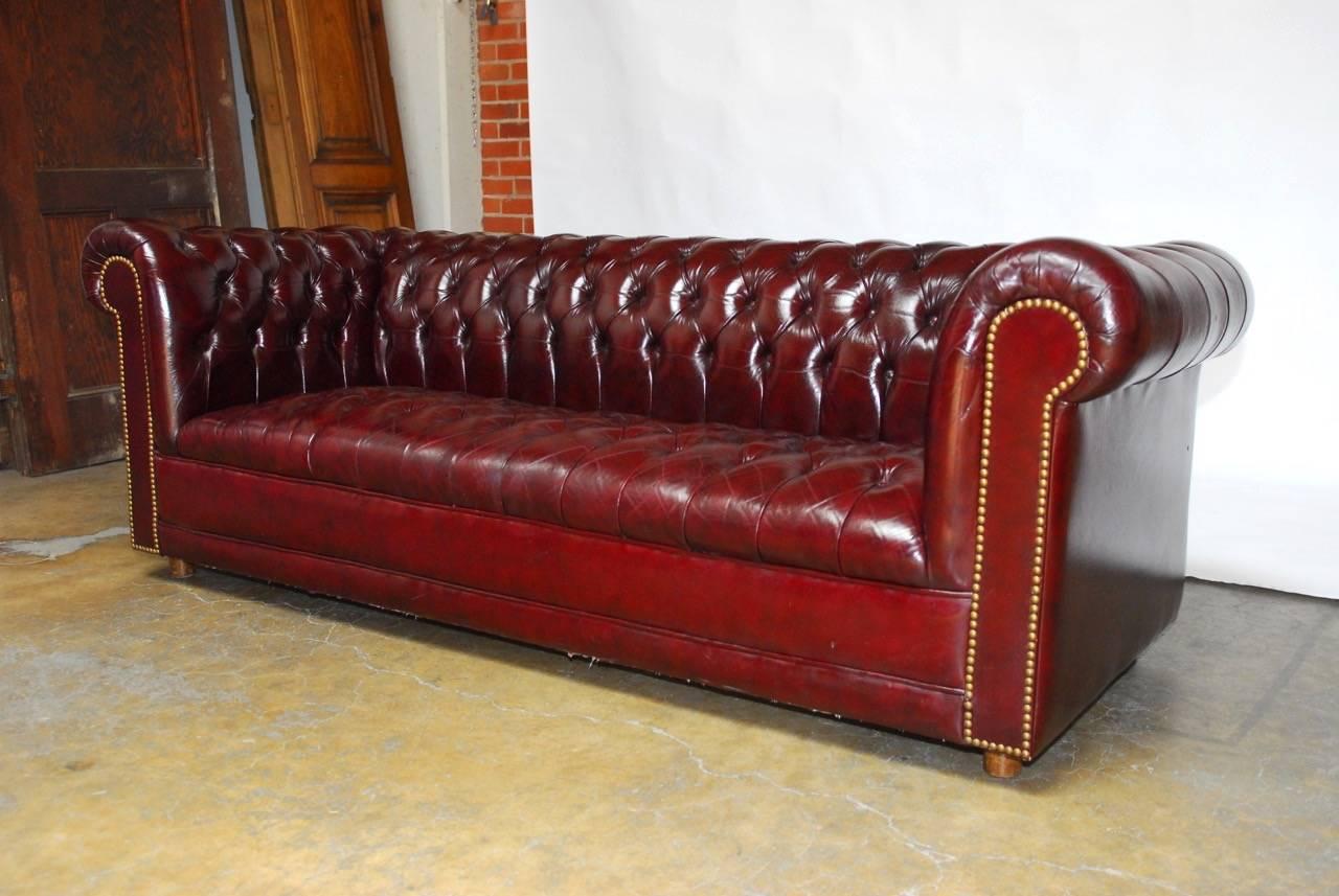 Classic English leather Chesterfield sofa featuring a soft, supple, shiny leather finished in a deep cordovan with a deep generous seating area. The seat, back and arms have all been tufted and the sofa has brass nailhead trim accents on the front
