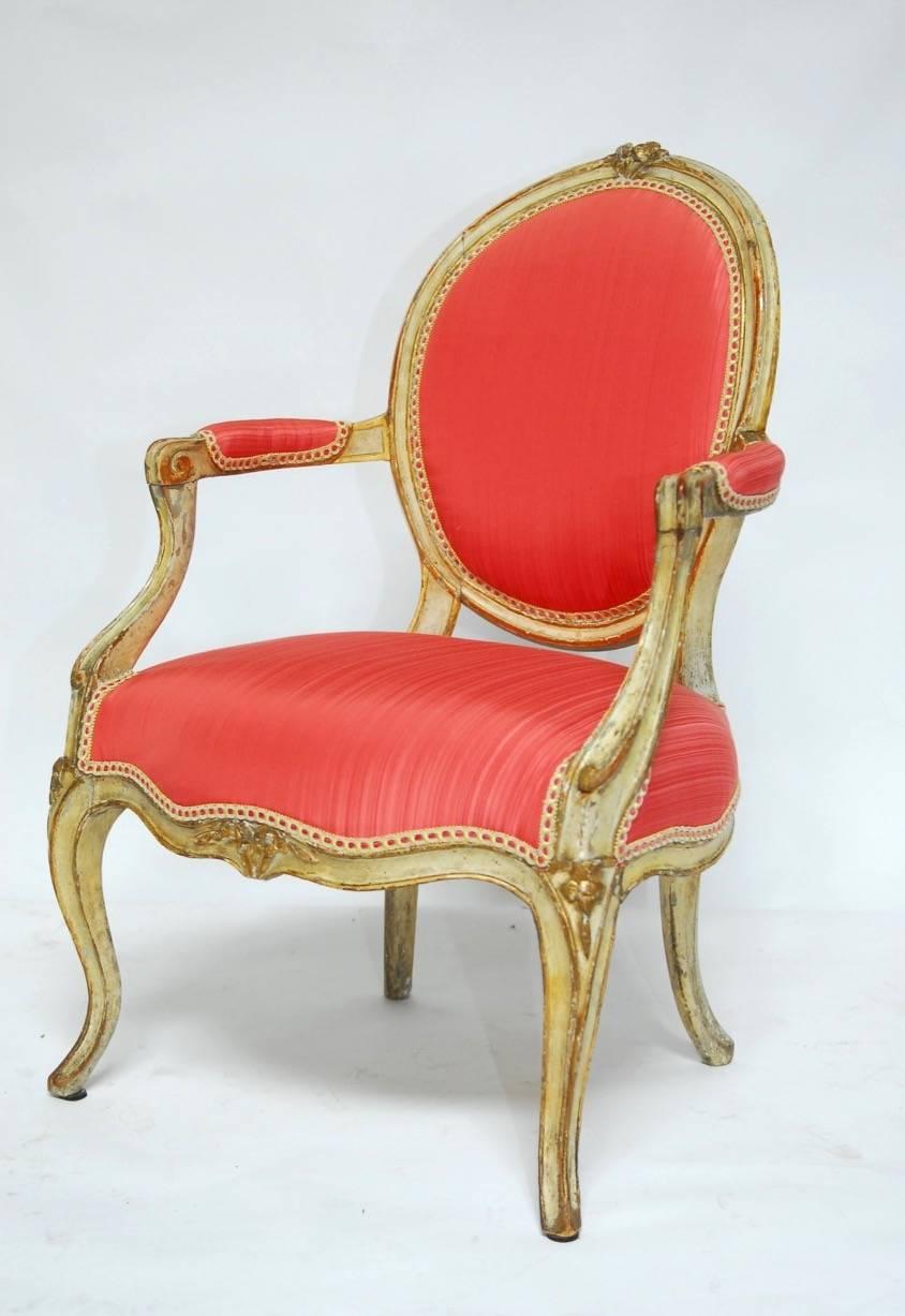 Fabulous pair of Louis XV period fauteuils featuring a painted and parcel-gilt distressed finish. Upholstered in a stunning salmon pink brocade. Beautifully molded frames with cabriole legs, floral crests, and an open exposed back. The front and