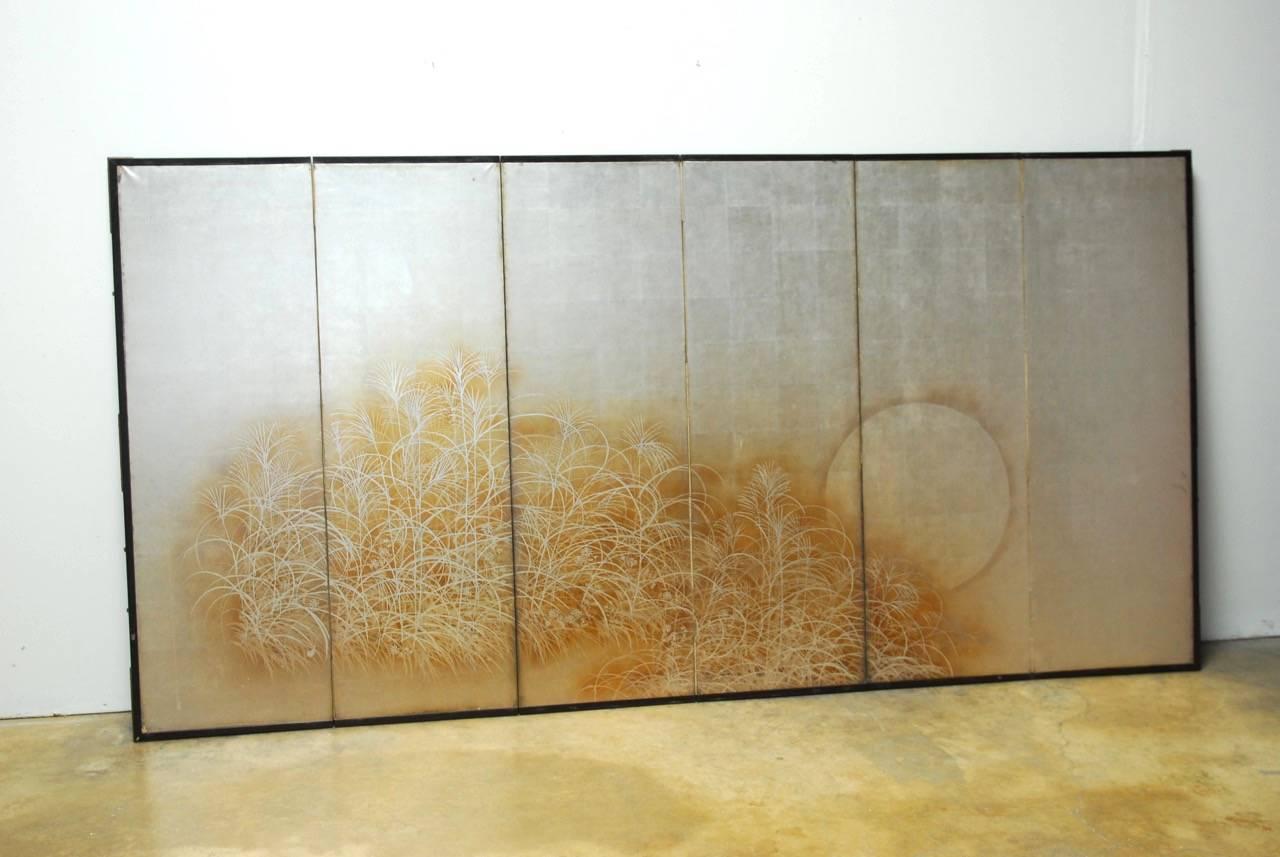 Captivating Japanese six-panel folding byobu screen featuring a hand-painted silver leaf finish decorated with eulalia grasses and delicate autumn daisies with a full moon rising in the background. Crafted from squares of silver leaf and set into an