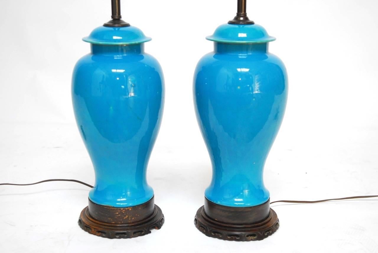 Rare pair of Chinese porcelain sky blue vases mounted as table lamps. Featuring a lidded ginger jar form and mounted on carved wooden plinths with brass hardware. Beautifully glazed in a sky blue, almost turquoise color probably converted in the