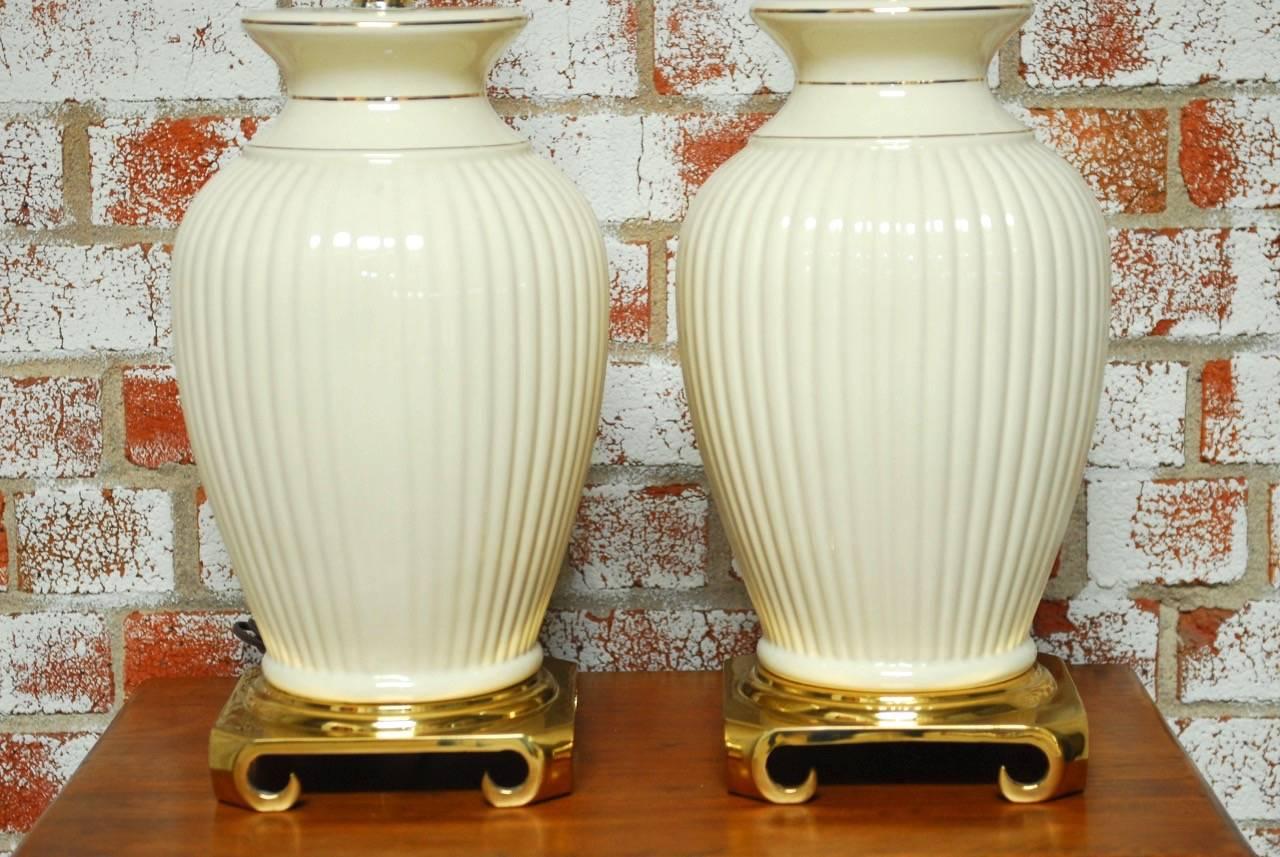 Elegant pair of Hollywood Regency brass and porcelain vase table lamps featuring a large ribbed base body decorated with gilt trim. Supported by a brass base with chow feet. Excellent condition with harps and finials but no shades. 