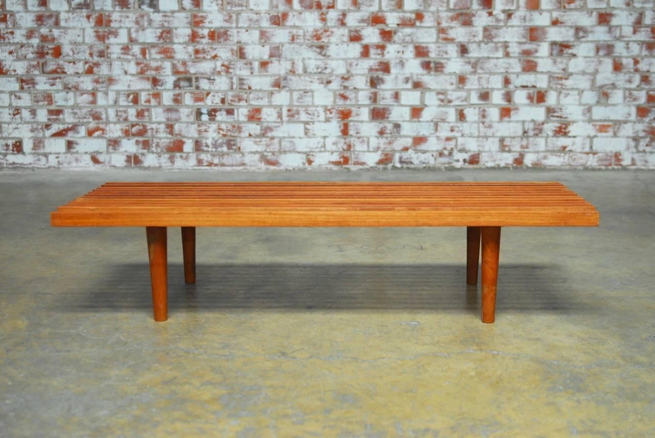 Sleek Mid-Century Modern low slat wood bench coffee table featuring a delicate slat wood top made in the manner of George Nelson. Simple Minimalist style supported by tapered round legs. Natural finish that showcases the lovely woodgrain.