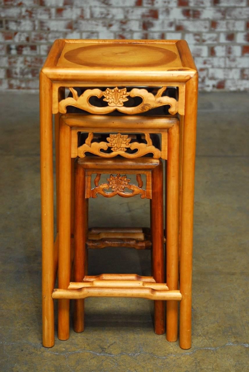 Large set of three carved Chinese nesting tables or stacking tables featuring a lotus blossom decoration on the apron and humpback stretchers. Each table is supported by round legs and have a beautiful faded patina. The tops were constructed with an