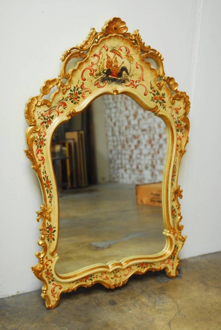 Stunning Italian Venetian style mirror decorated in the chinoiserie taste featuring a hand-carved frame finished with an ivory lacquer ground. Decorated with carved scrolls and surmounted by a shell crest. Hand-painted with an Asian motif and