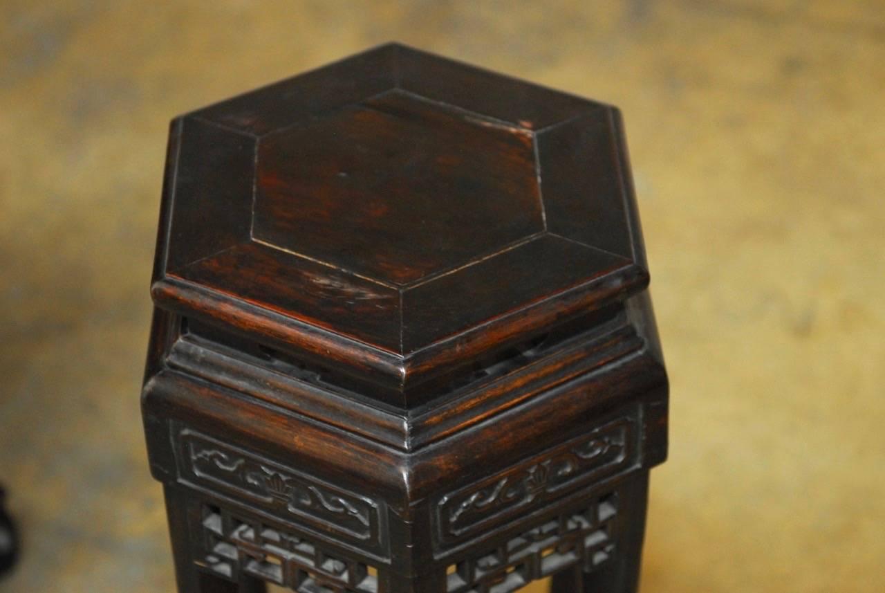 Remarkable pair of Chinese carved pedestal tables or plant stands featuring an ebonized lacquer finish. Hexagonal shaped floating top panel with a pierced open fretwork decoration on the aprons. Supported by six elegant legs that hold a bottom