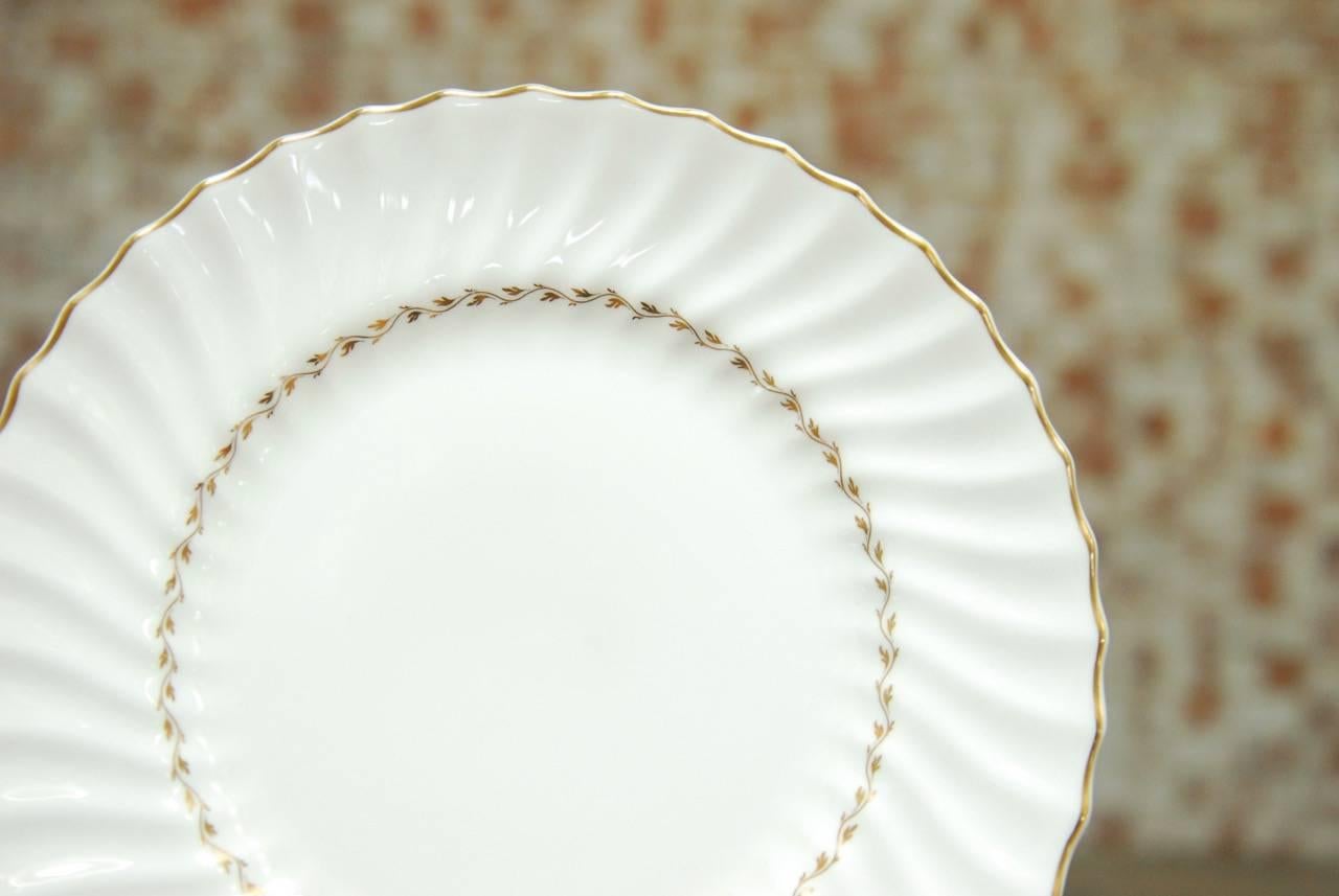 Set of 12 exquisite Royal Doulton English porcelain dinner plates in the Adrian style. This set of 12 bone china dinner plates features a scalloped edge with a gilt band with an inner band of laurel leaves. Timeless and elegant never goes out of