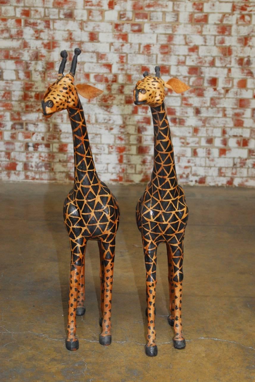 Charming pair of hand-painted leather giraffe sculptures featuring a geometric pattern body and life like heads with glass eyes. Similar size with one being slightly larger. Beautifully crafted in excellent condition.