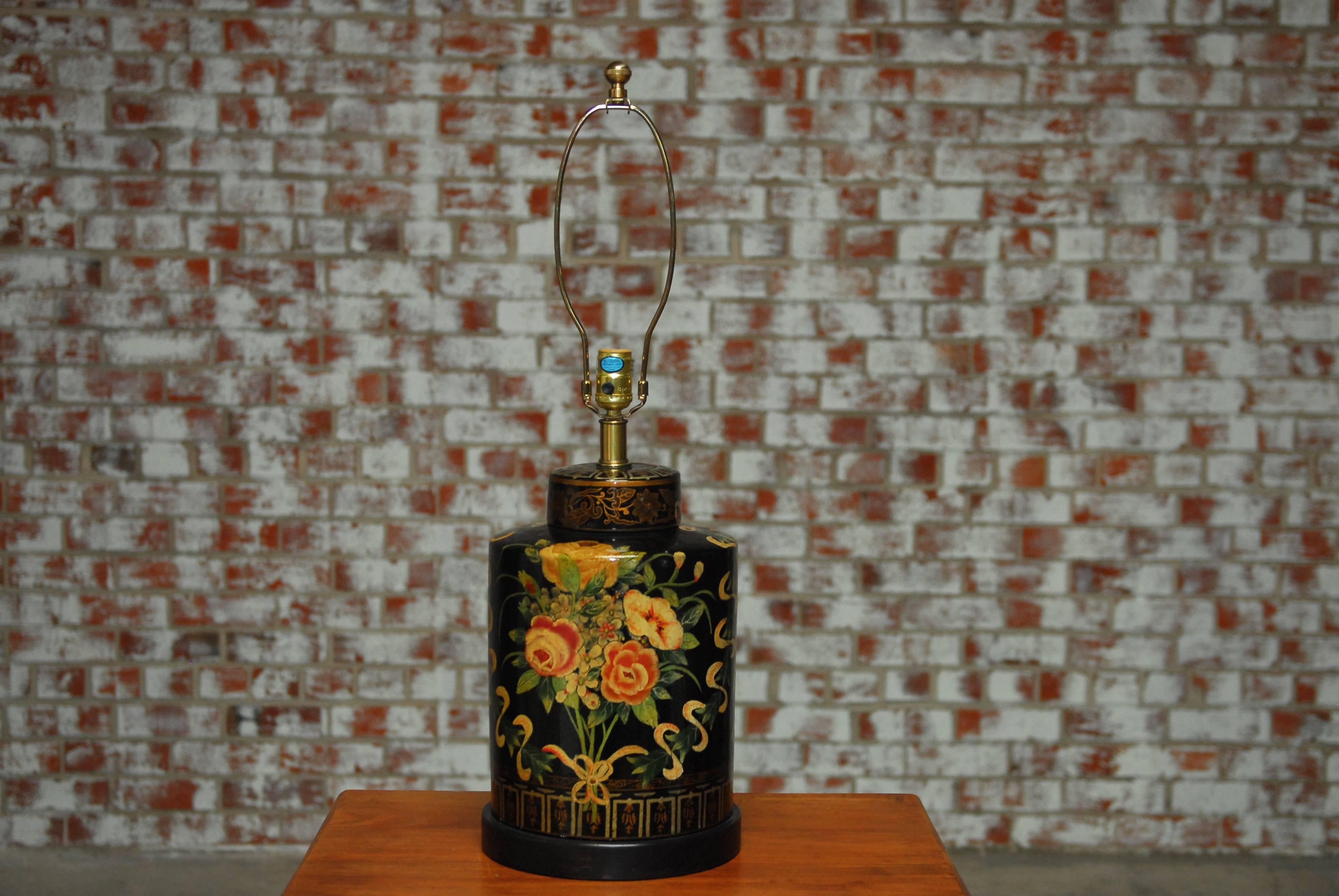Frederick Cooper vintage black floral tea canister ceramic lamp featuring a floral and swag motif, craquelure finish with brass hardware and hand-painted gilt accents. Topped with brass hardware and a round finial. Supported by a round ebonized wood