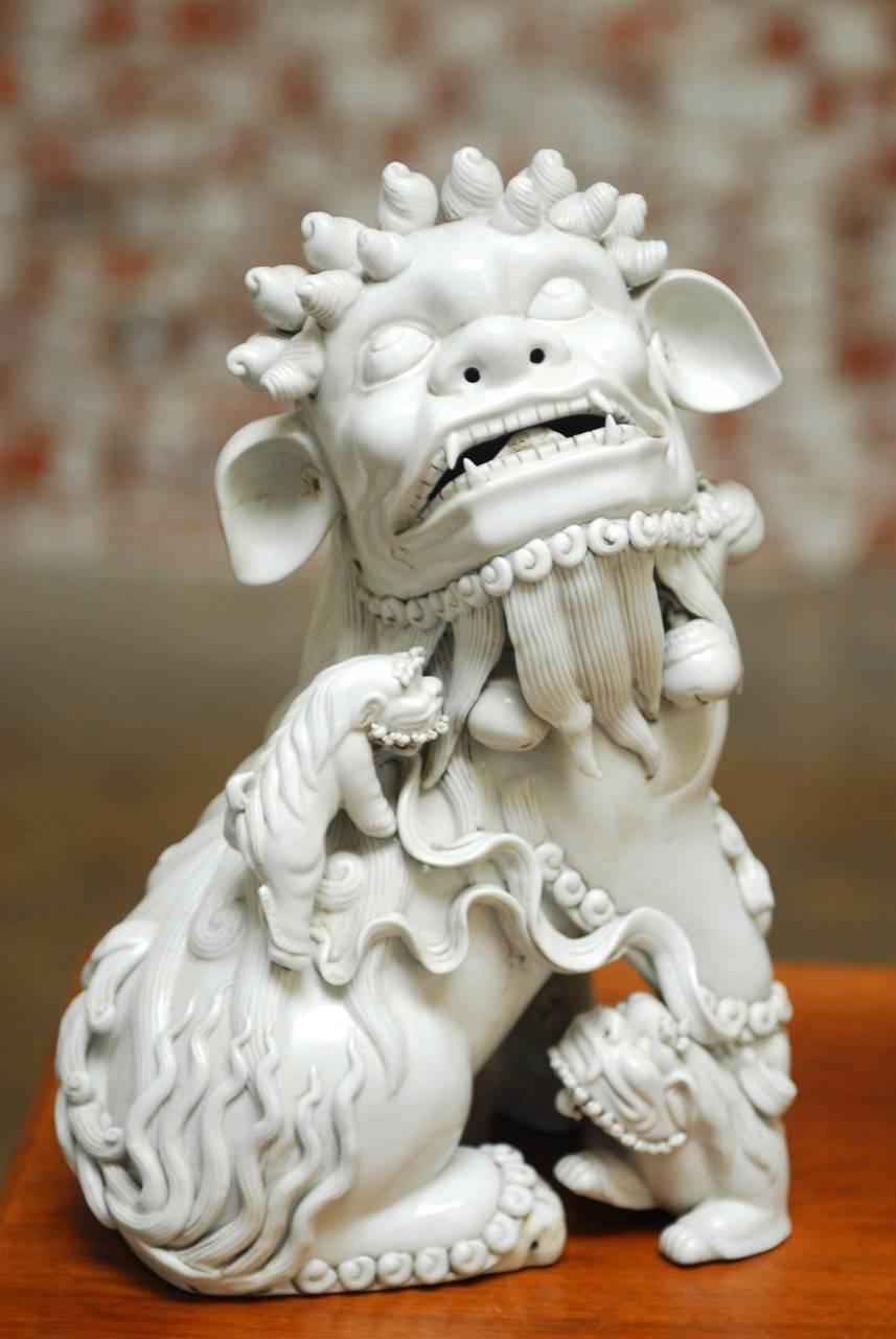 Fantastic pair of Chinese Dehua blanc de chine porcelain foo dogs. Featuring intricate decoration and detail. Depicted sitting one male, and one female holding a cub and a ball. Their heads are covered with tight snail curls and they each have three